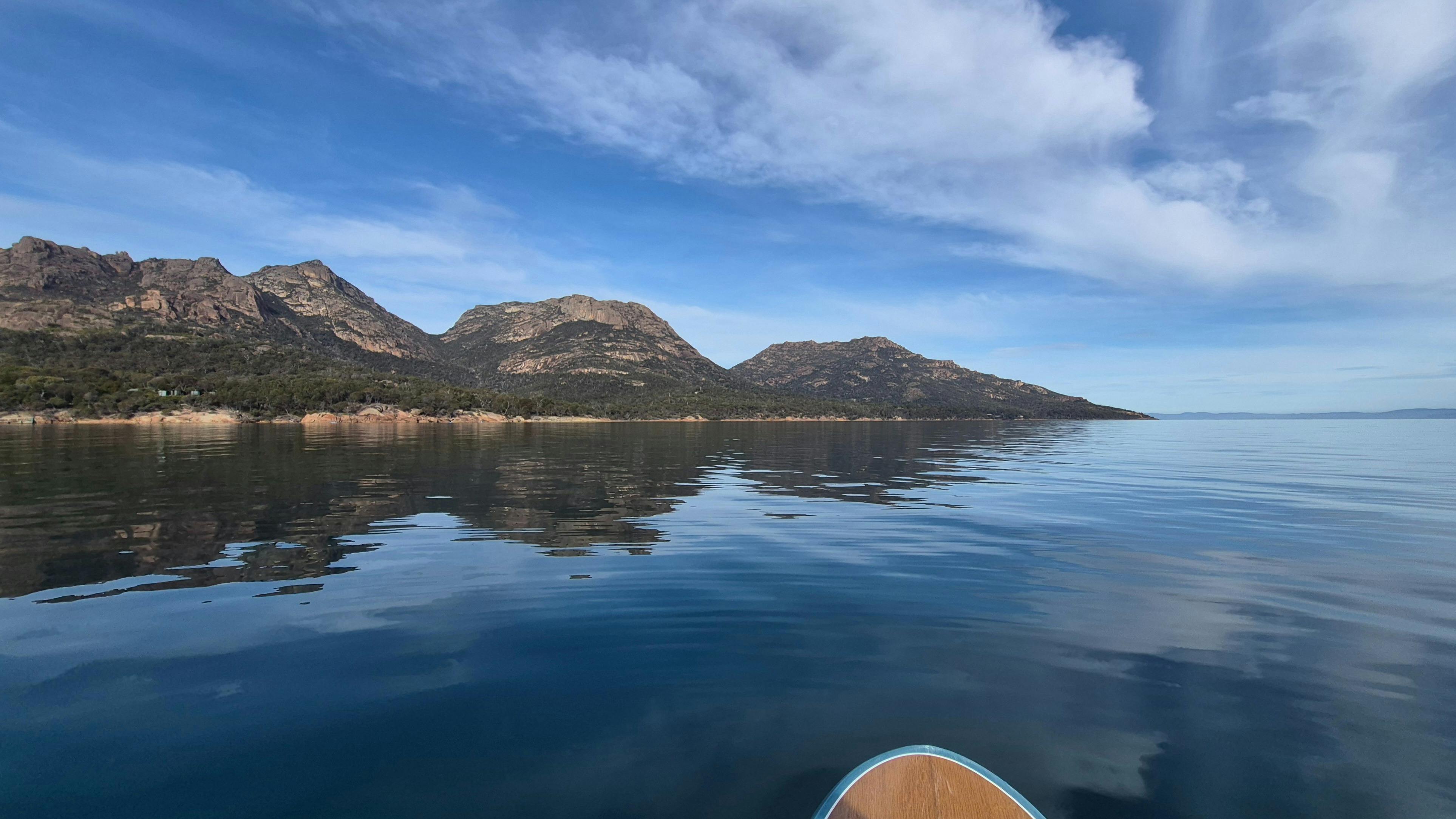 Paddleboarding on glassy, calm conditions in  Coles Bay in Tasmania, against the scenic Hazards.