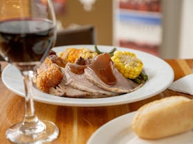 A plate with roast meal, veggies and glass of red wine.