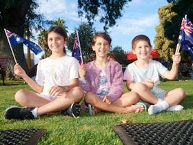 Three children sit together waving Australian flags