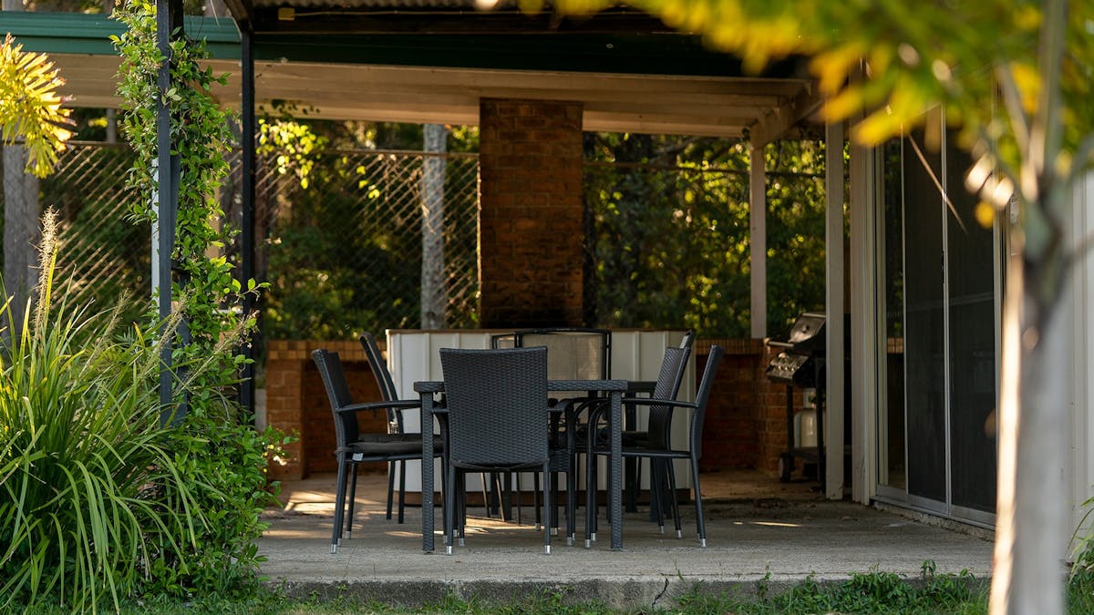 Table and chairs with a gas BBQ in the backgound.