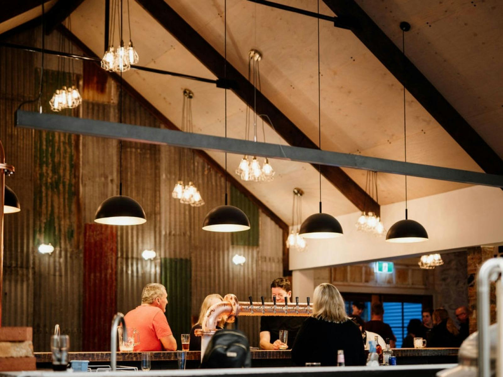 Warm brewery interior with patrons seated at bar beneath hanging pendant lights.