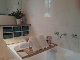 Bath, bath caddy over bath, champagne glass, book, bath salts, towels and potted plant.
