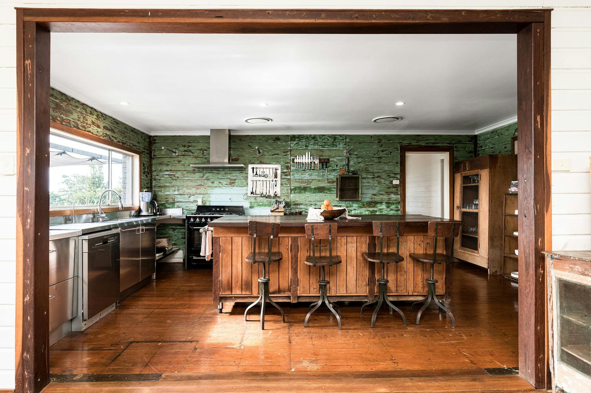 A kitchen with deep green wall and timber island bench with four stools.