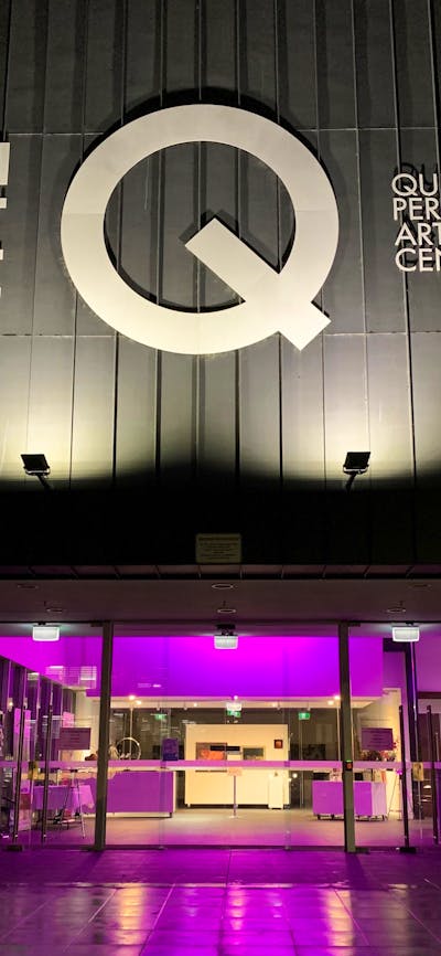 Façade of building with large white lettering and internally lit with purple lights