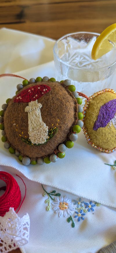 Fabric decorative hangers embroidered with mushrooms next to a gin and tonic