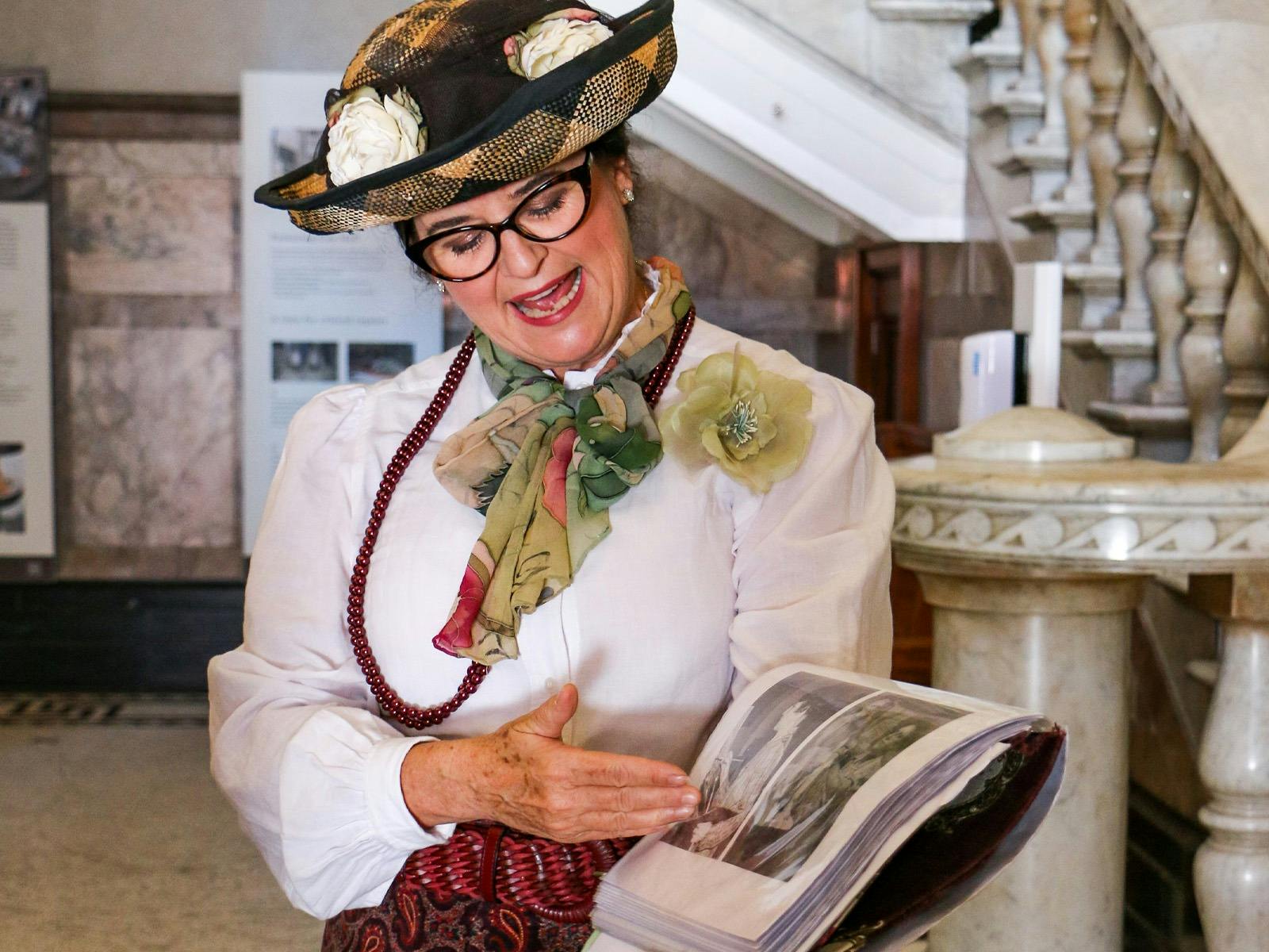 A woman dressed in old timey clothing gestures to book standing in foyer of city hall