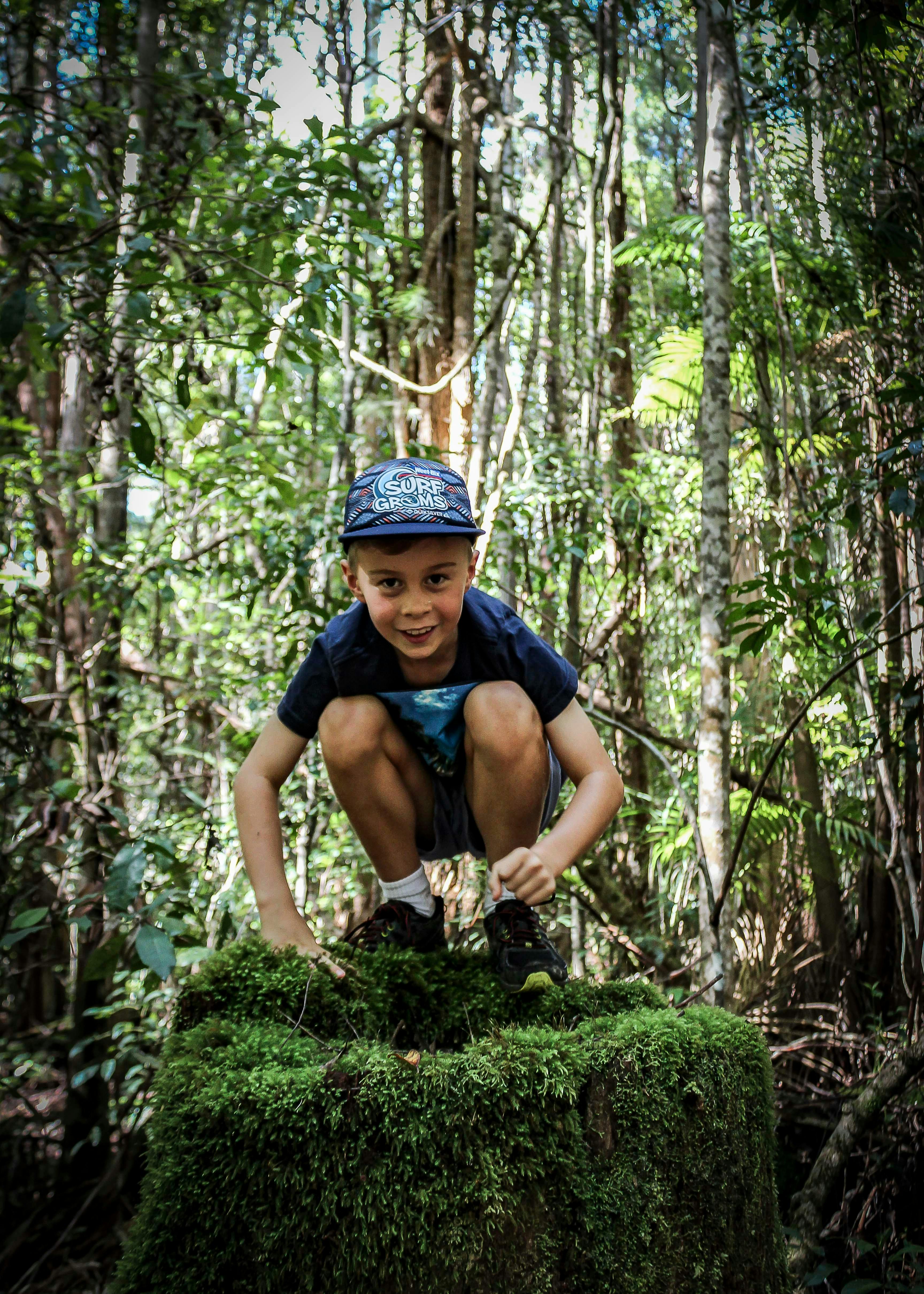 A small boy perches on top of a mossy log