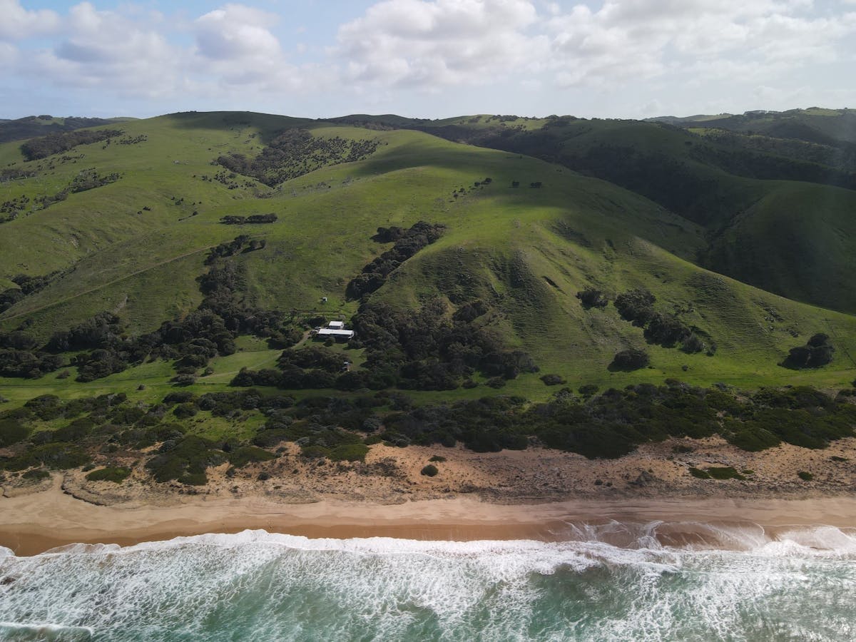 Drone view looking over the ocean, beach, house and green hills beyond
