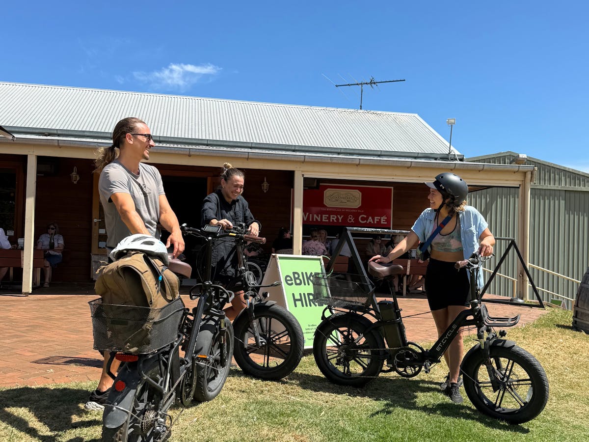 Three young adults laughing as they lean on their eBikes outside Oxenberry Farm Cellar Door