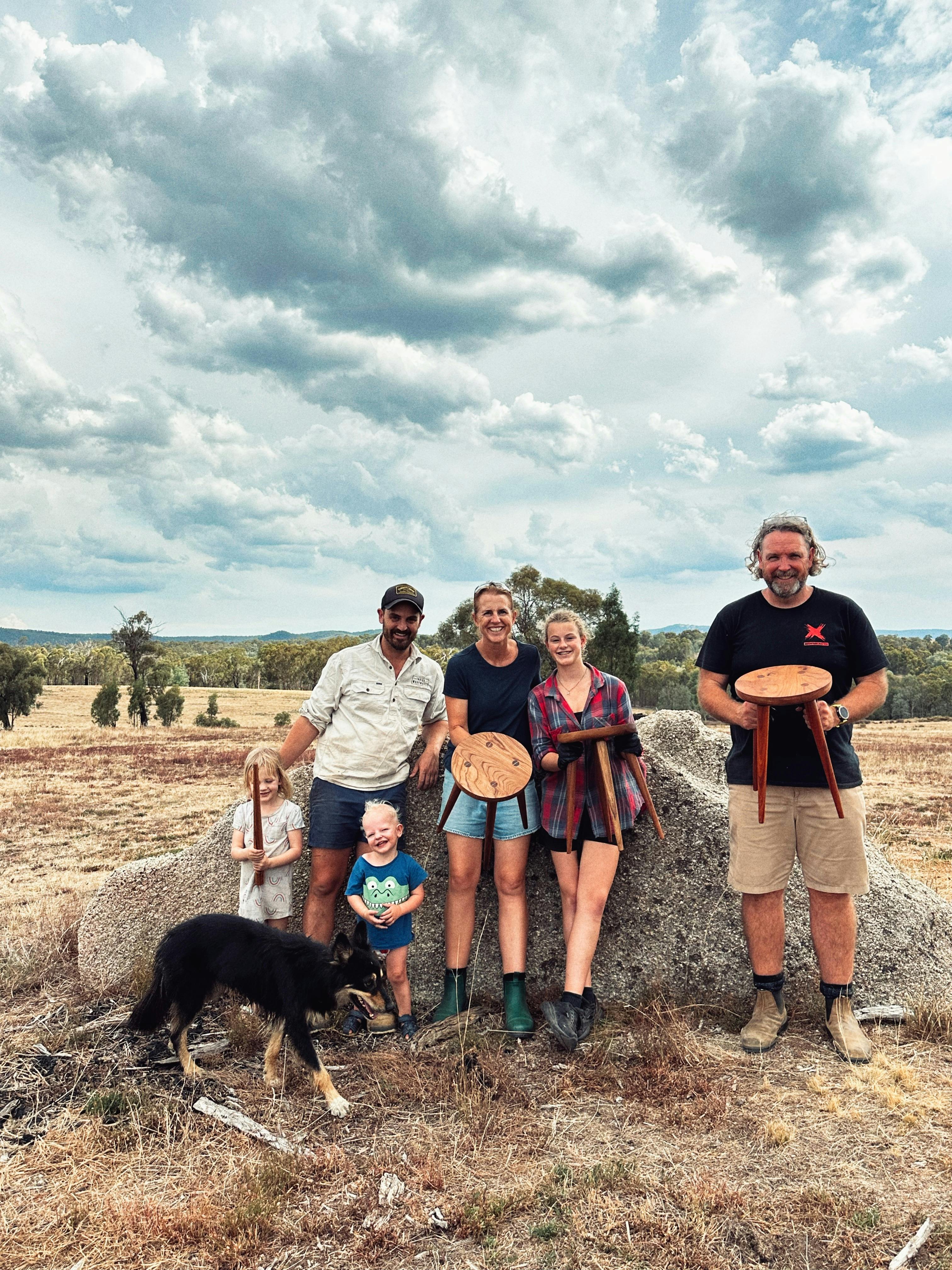Three participants hold their stools in front of a rock