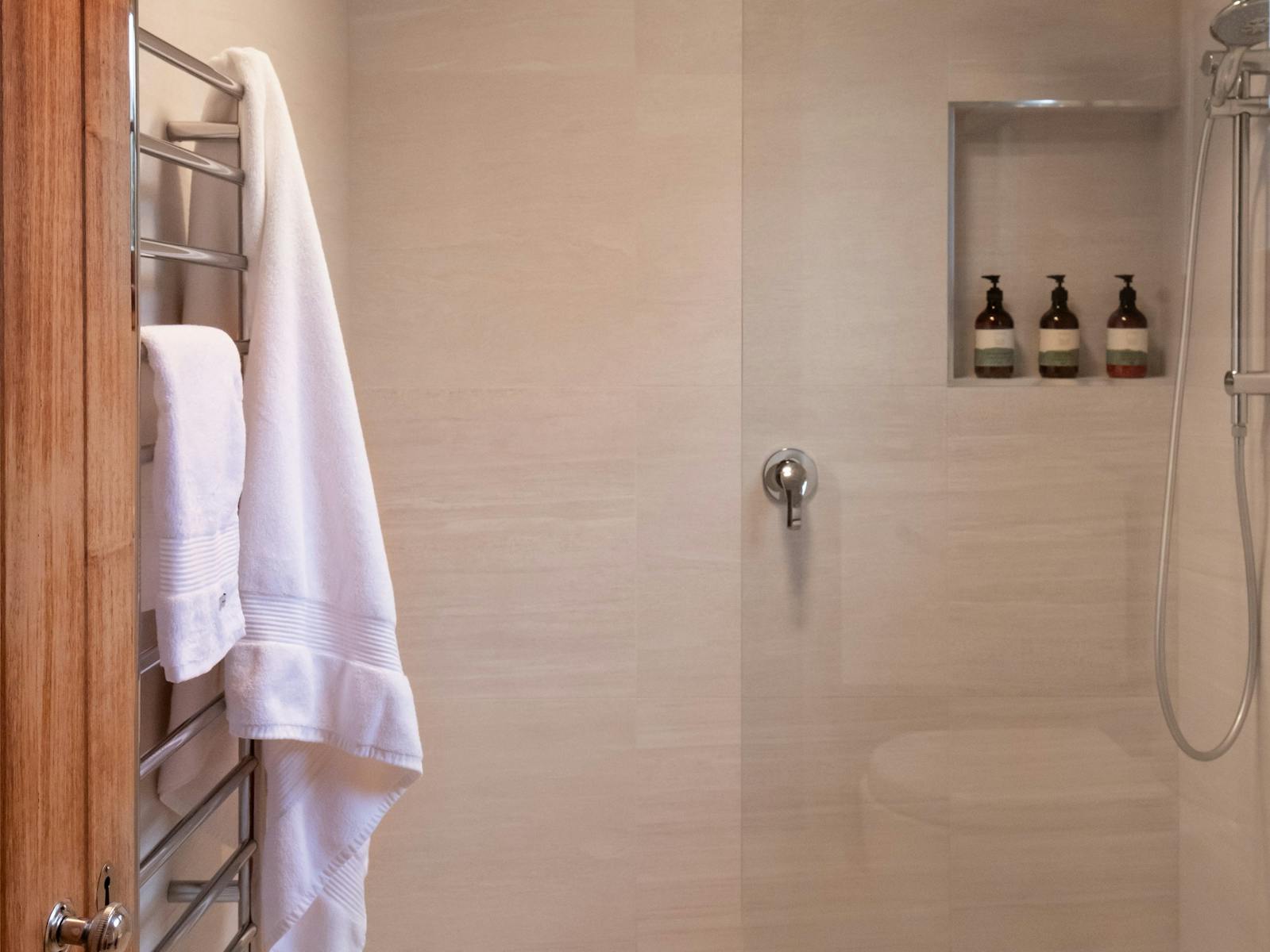 Tiled bathroom with walk-in shower, built-in nook, towel rail with bath sheets hanging from it
