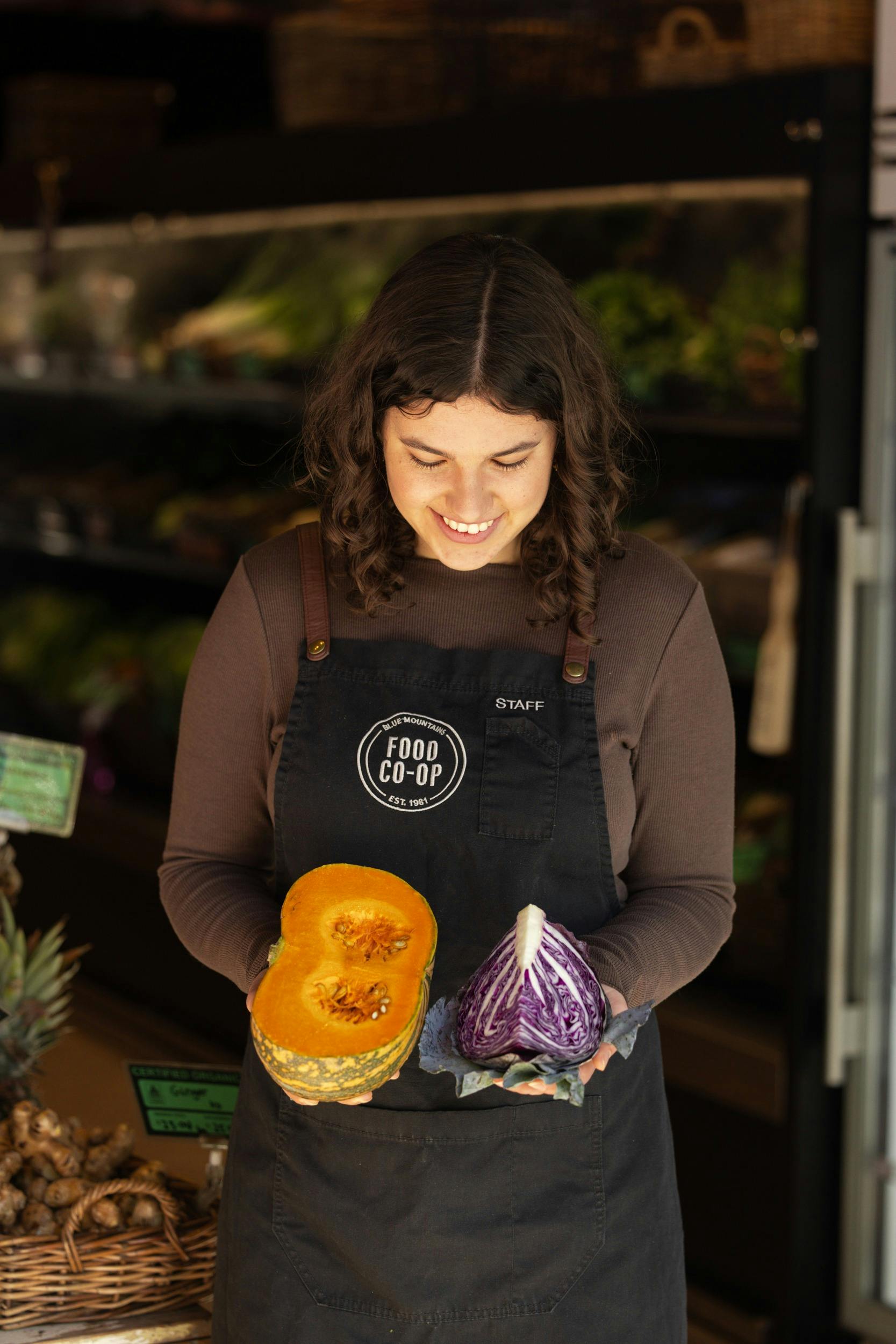Smiling staff member wearing apronholding half a pumpkin and a quarter of a purple cabbage