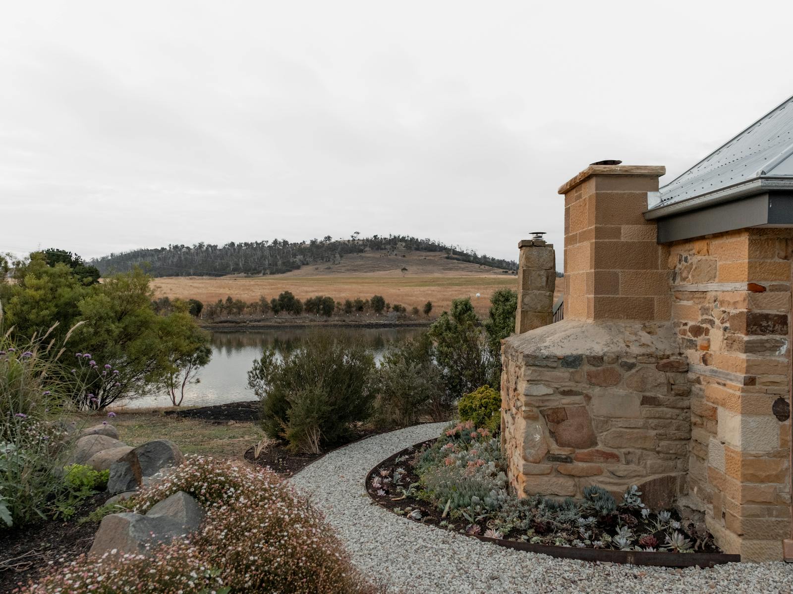 on the right two sandstone chimneys, a curve path through centre of image , garden and river behind