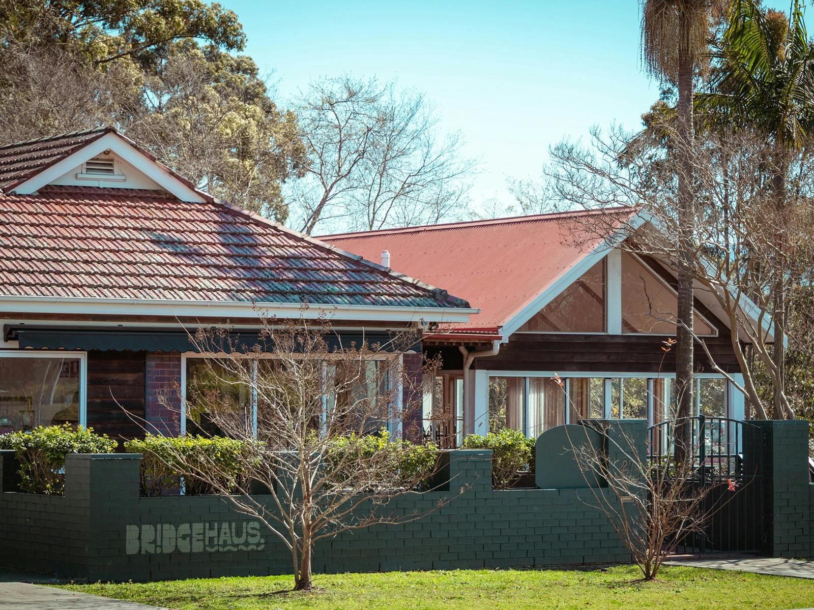 BridgeHaus exterior with dark timber cladding, red roofs, large windows and a green garden wall.