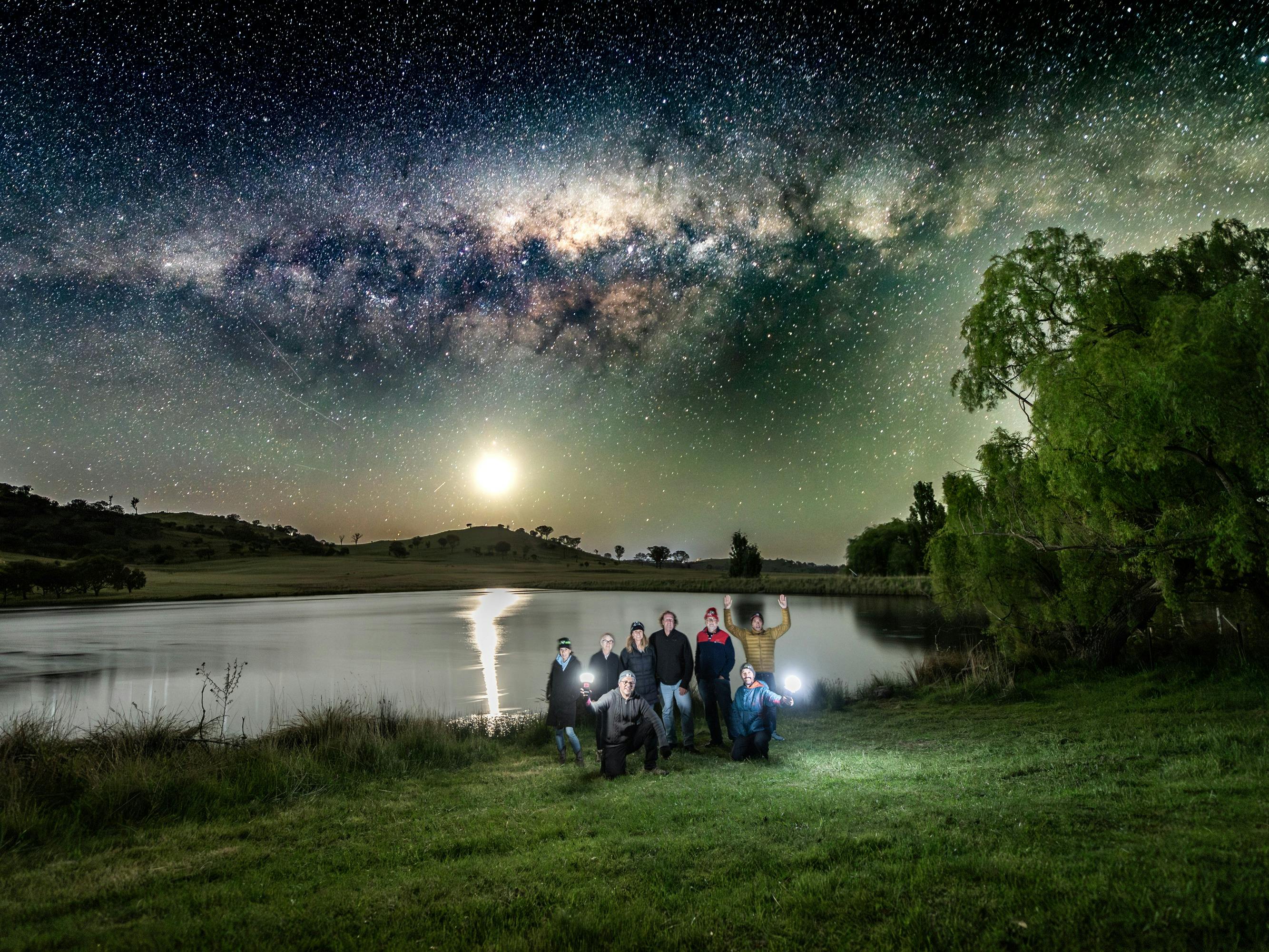 A portrait of a group of partecipants with Moon and Milky Way reflecting over a lake