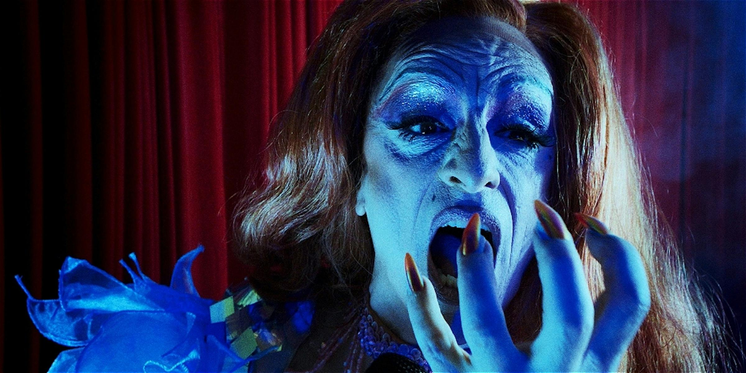 Lady is lit up in blue lighting as she screams with her hand to her mouth.