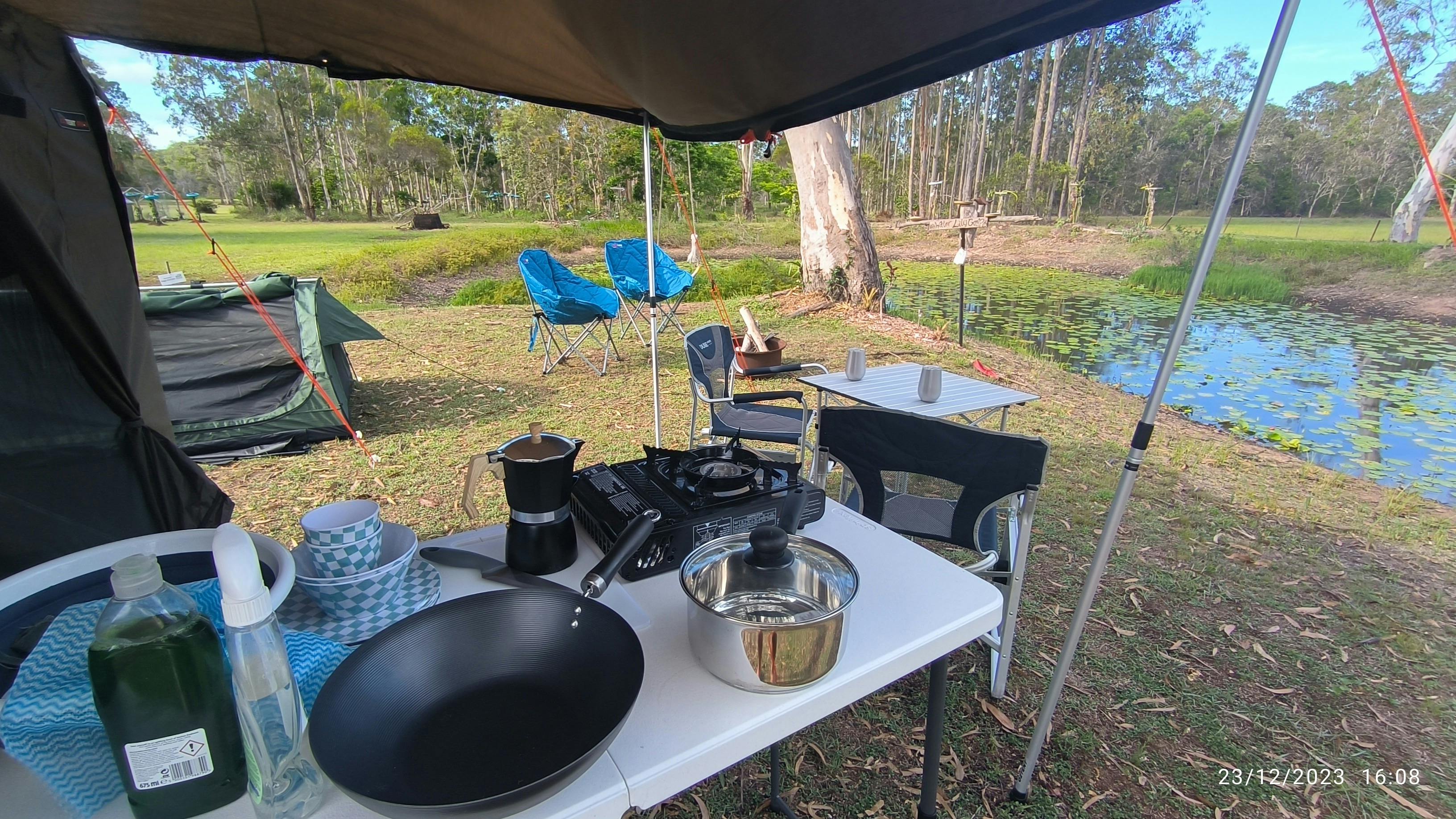 kitchen setup under the awning of a safari tent overlooking a dam