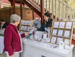 A stationary market stall, the artist is smiling and handing over a handmade card to the customer.