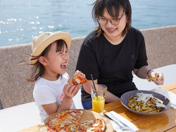 Young girl with her Mum enjoying pizza by the harbour