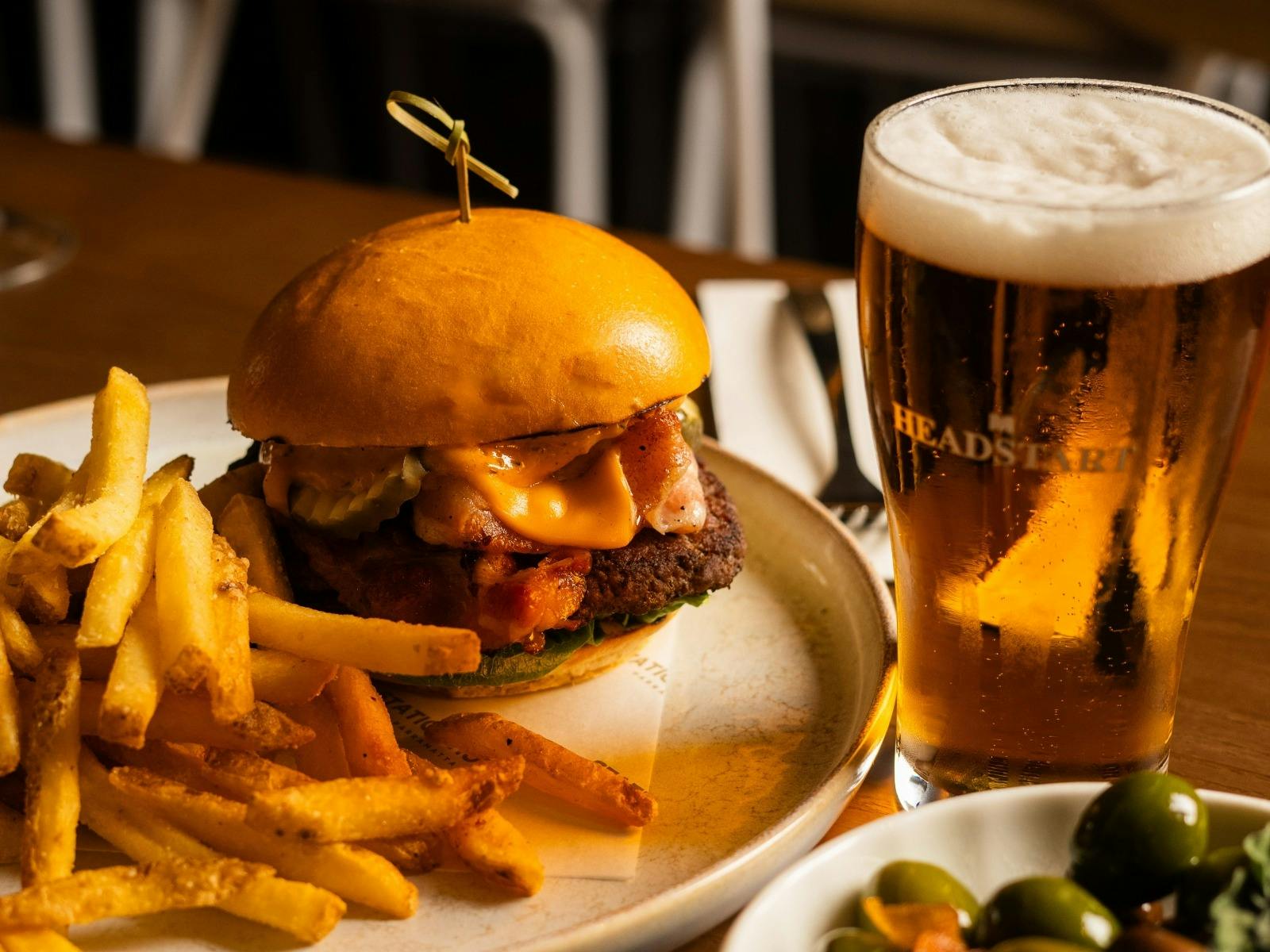 image of a burger, chips and a beer on a table