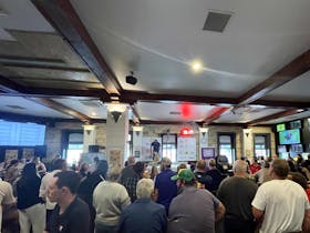 Shearer shearing a sheep in front of many people in a front bar of a hotel