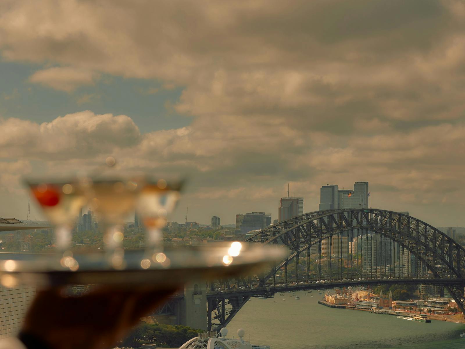 Waiter holds three cocktails in front of the view of the Sydney Harbour Bridge