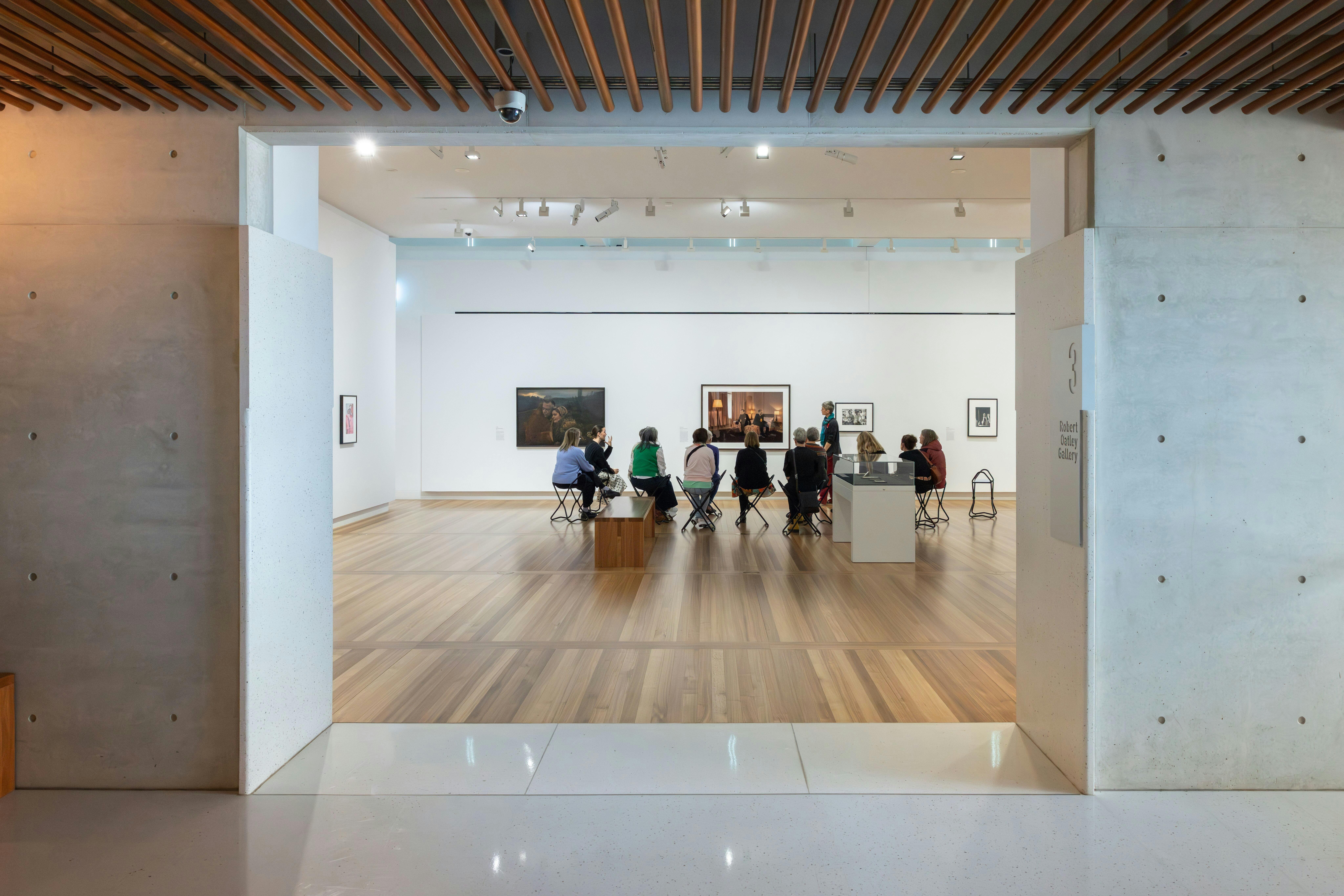 A group of people are seated in a brightly lit gallery, discussing portraiture with a guide.