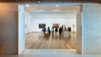 A group of people are seated in a brightly lit gallery, discussing portraiture with a guide.