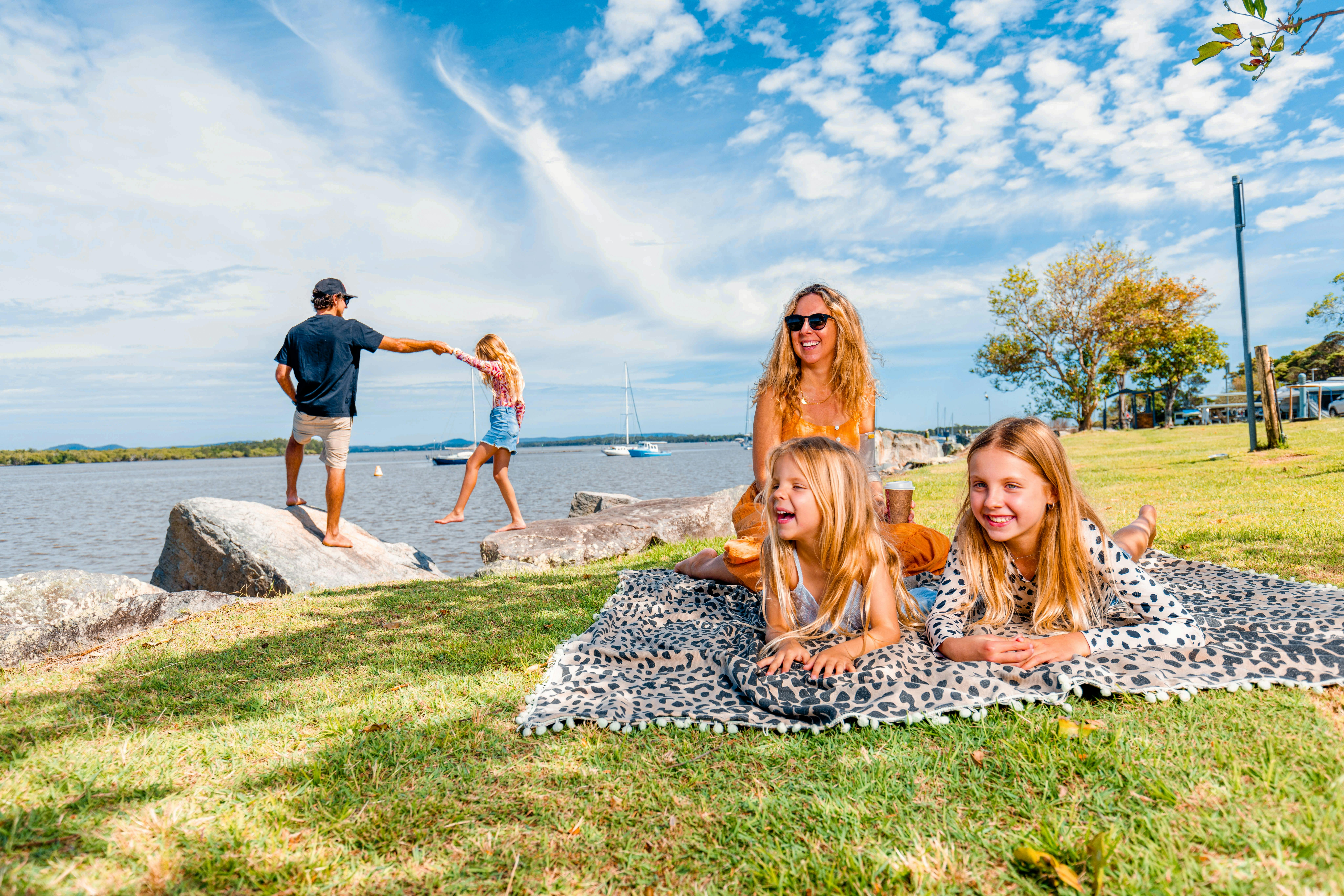 Eine Familie lacht lachend auf einer Picknickdecke am Flussufer.