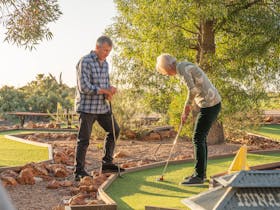 A couple are playing mini golf. It is