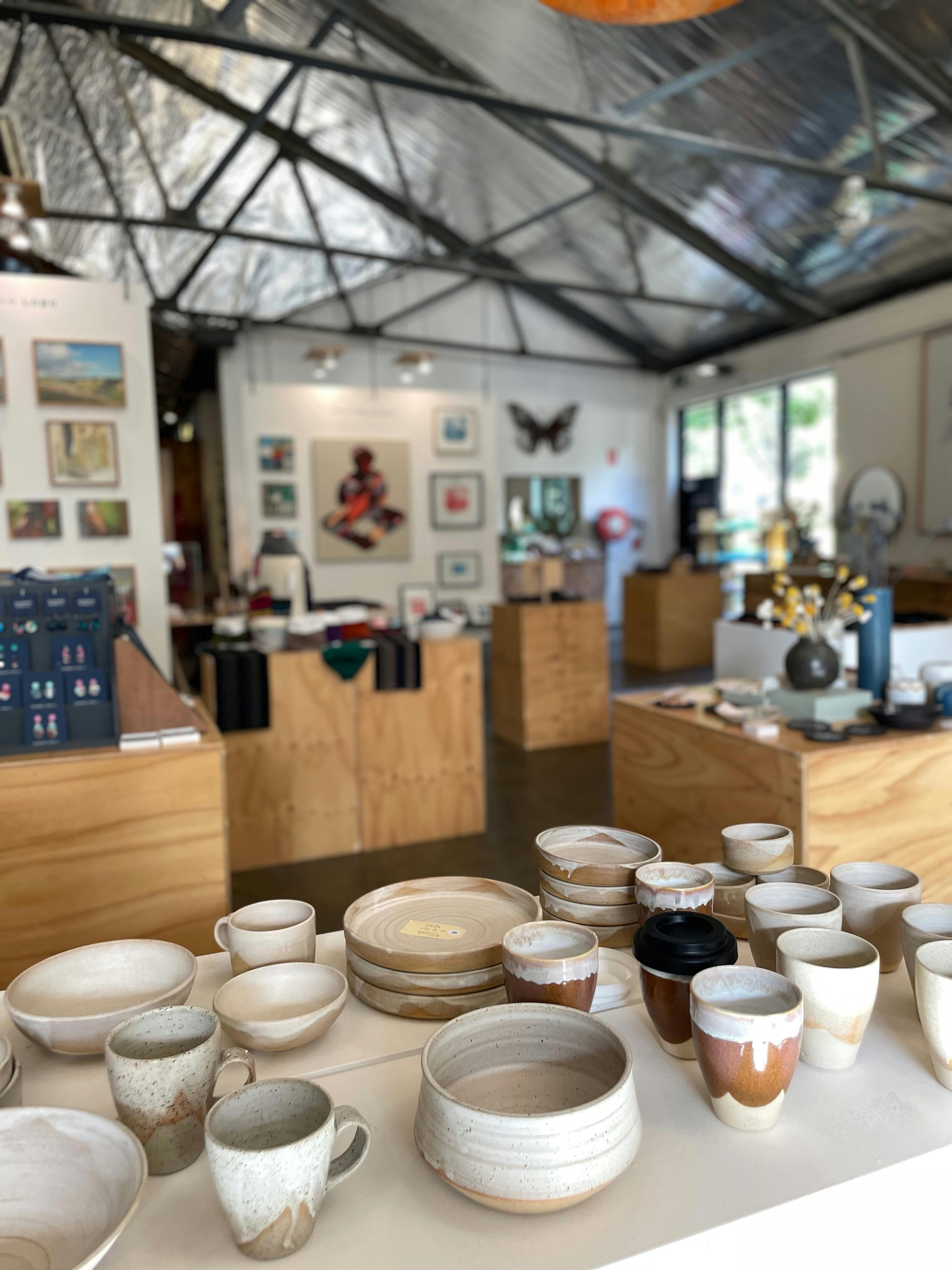 A close up of a plinth with ceramics cups and bowls with a blurry photo of a room