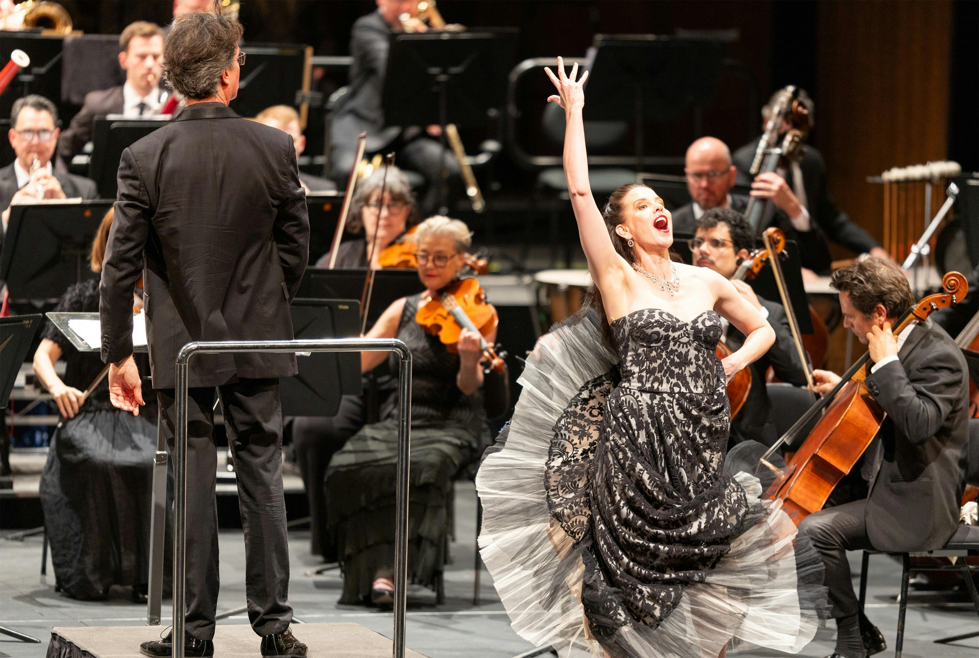 a woman singing strikes a pose in front of an orchestra