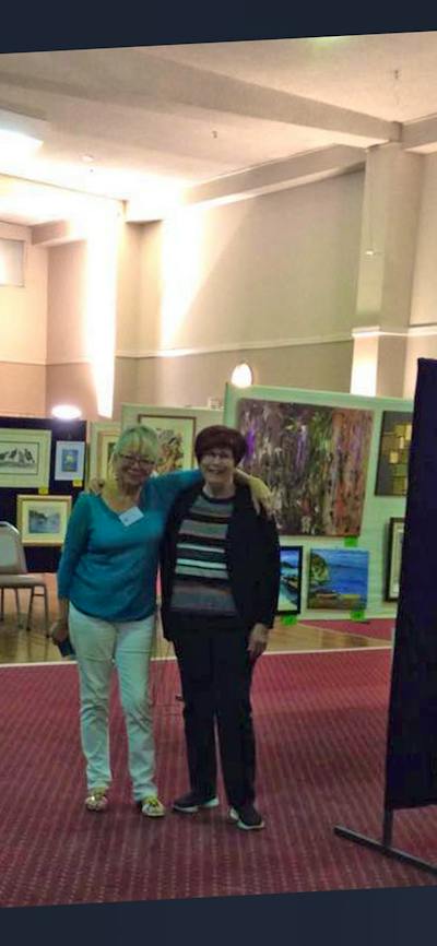 two ladies standing in the hall with art work on display around them.
