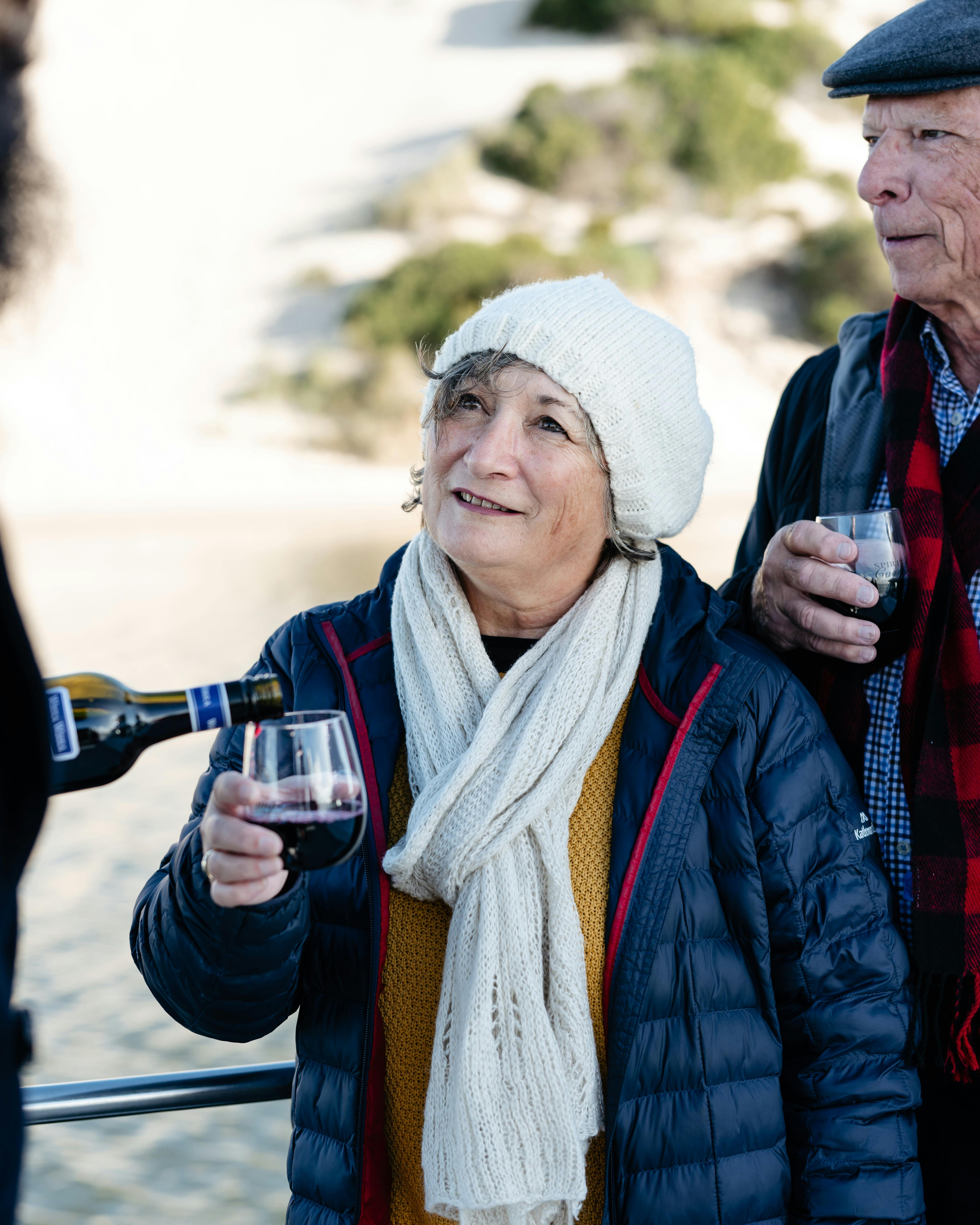 A person having their wine glass topped up. Wearing a scarf and beanie.