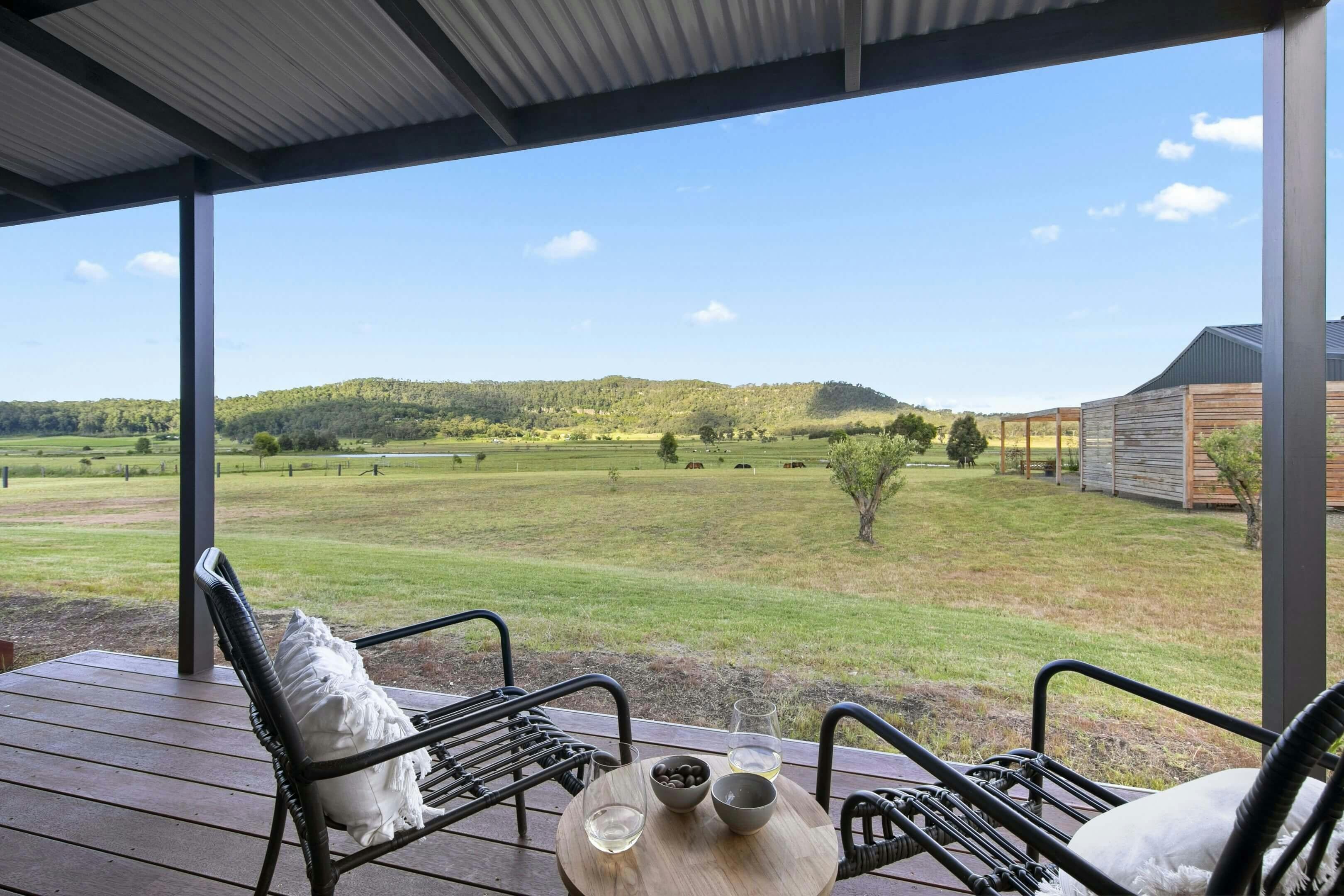 black chairs with white cushions and a small round table sit on a wooden porch overlooking a grass