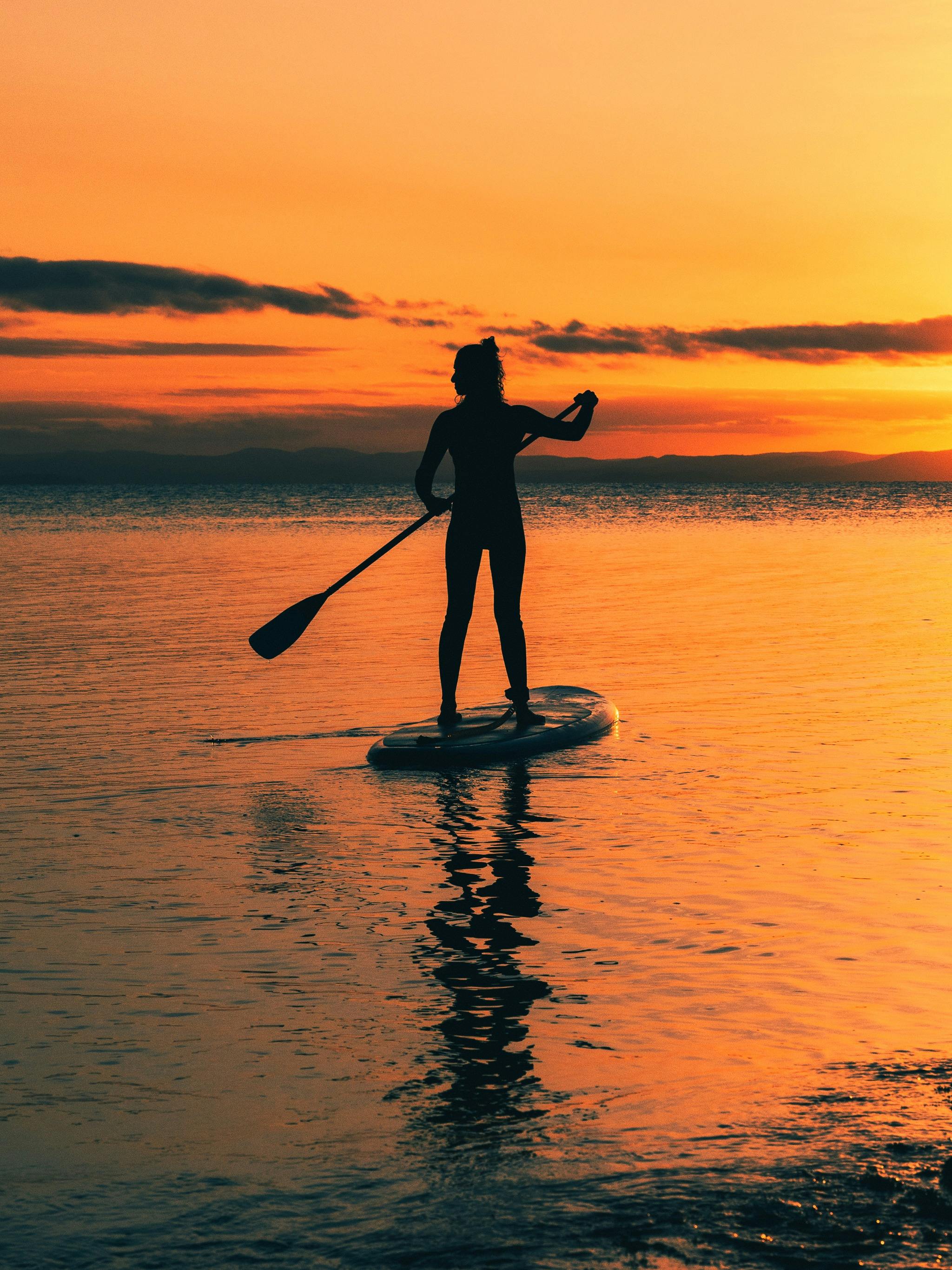 Vivid orange sunset with a women paddleboarding in Coles Bay/ Freycinet, Tasmania