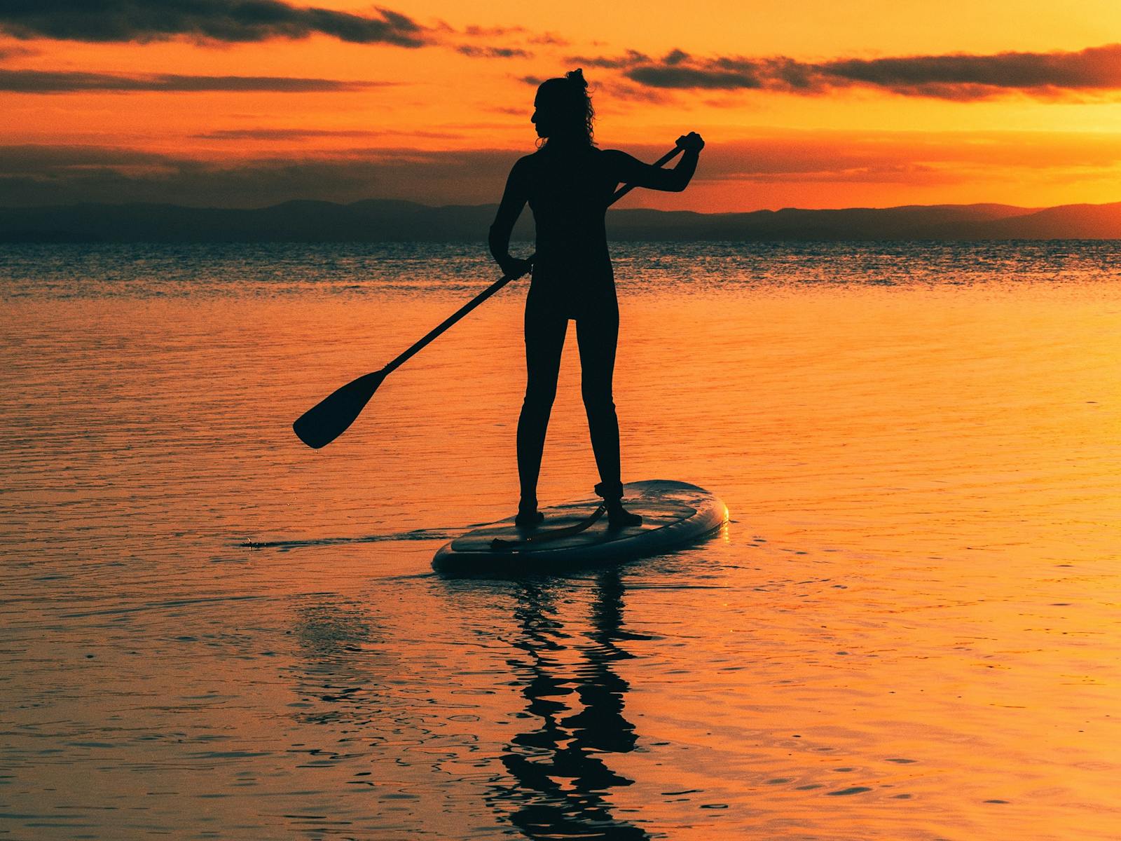 Vivid orange sunset with a women paddleboarding in Coles Bay/ Freycinet, Tasmania
