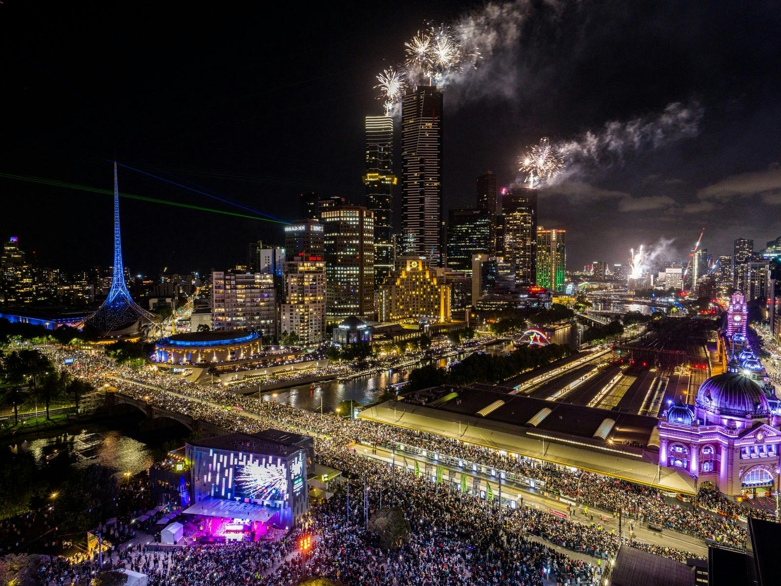 Fireworks explode around Melbourne CBD at night time. The Princess Bridge and Yarra River are in sho