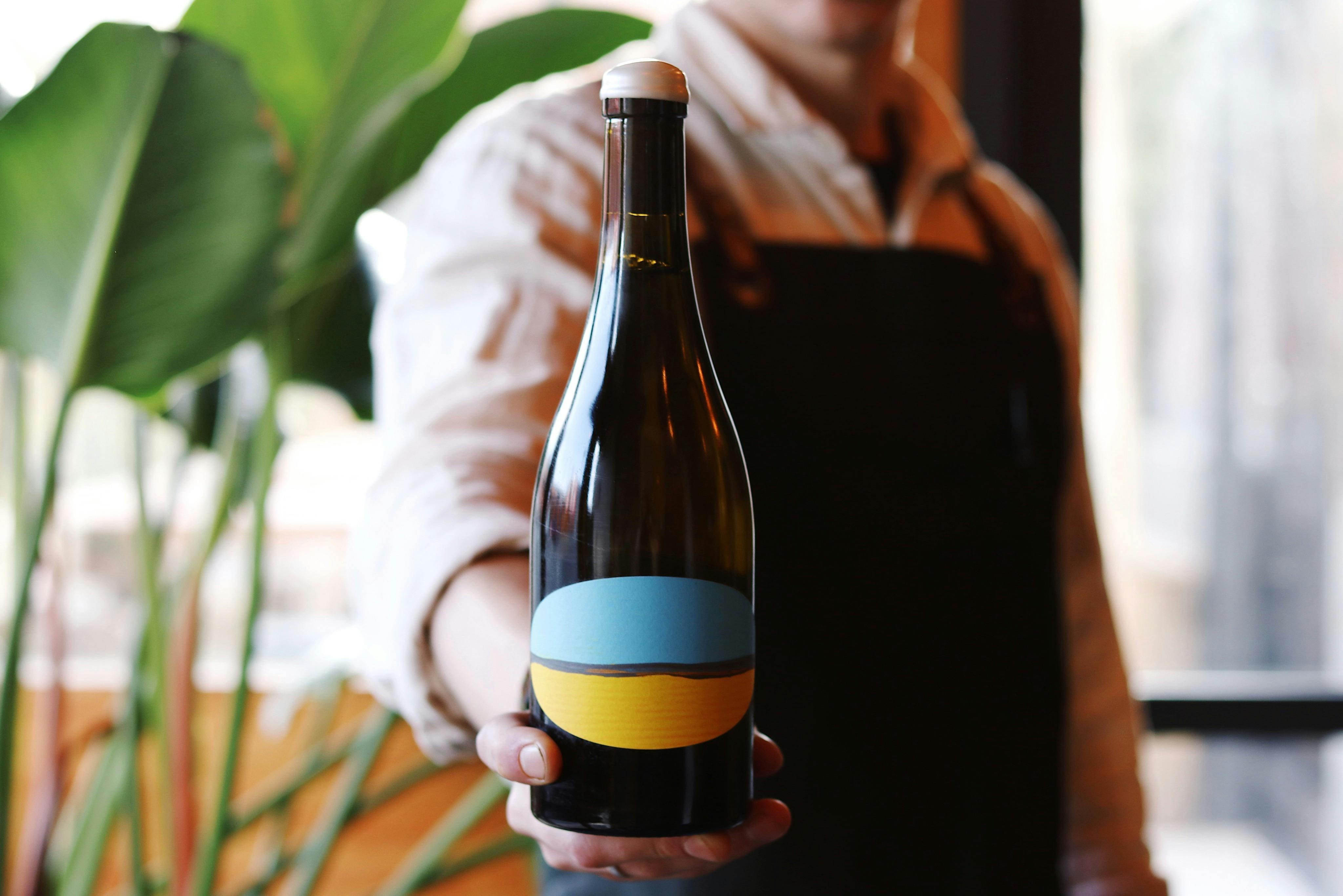 Close-up photo of a wine bottle with a blue and yellow label held by waitstaff (face not visible)
