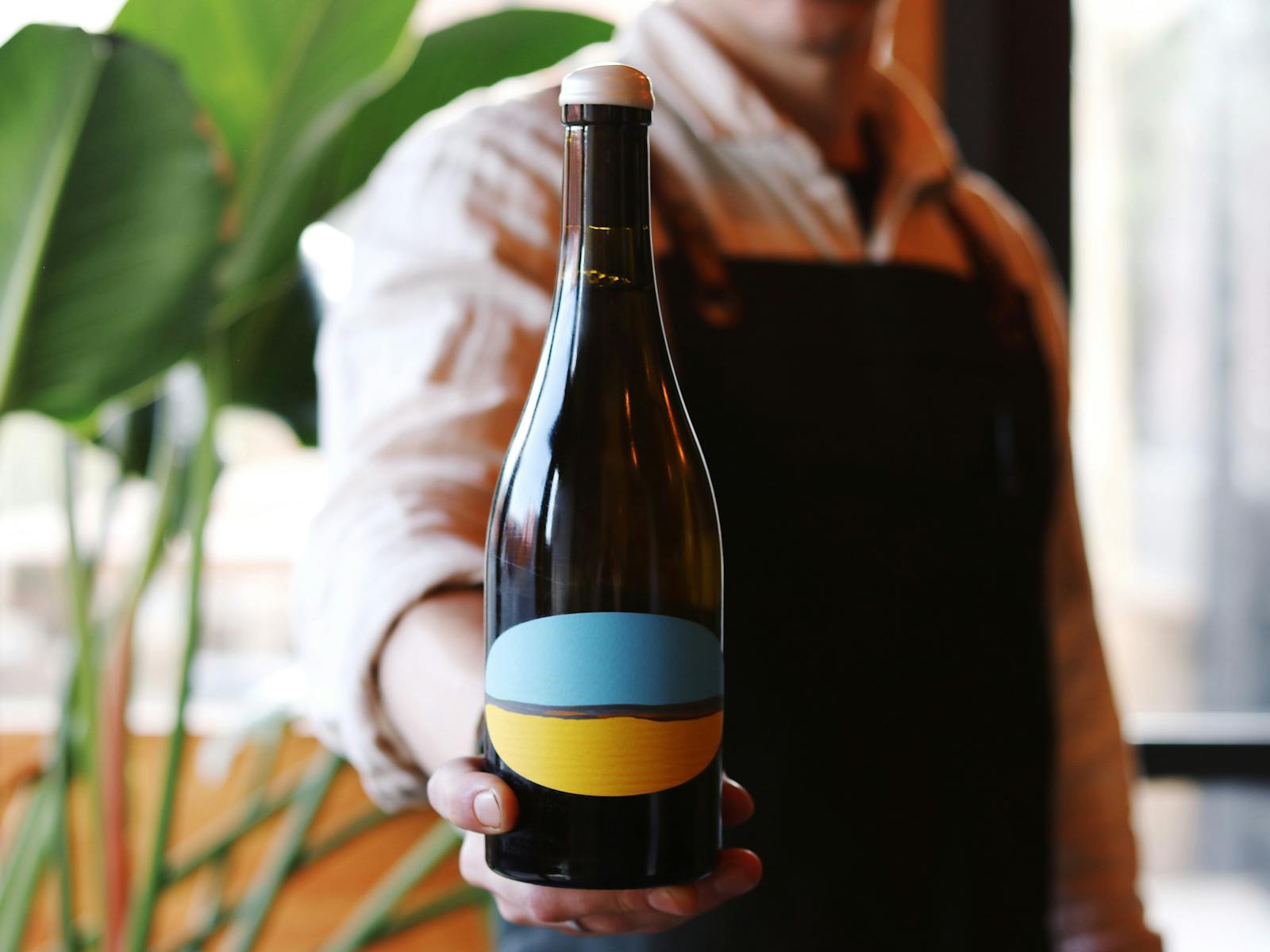 Close-up photo of a wine bottle with a blue and yellow label held by waitstaff (face not visible)