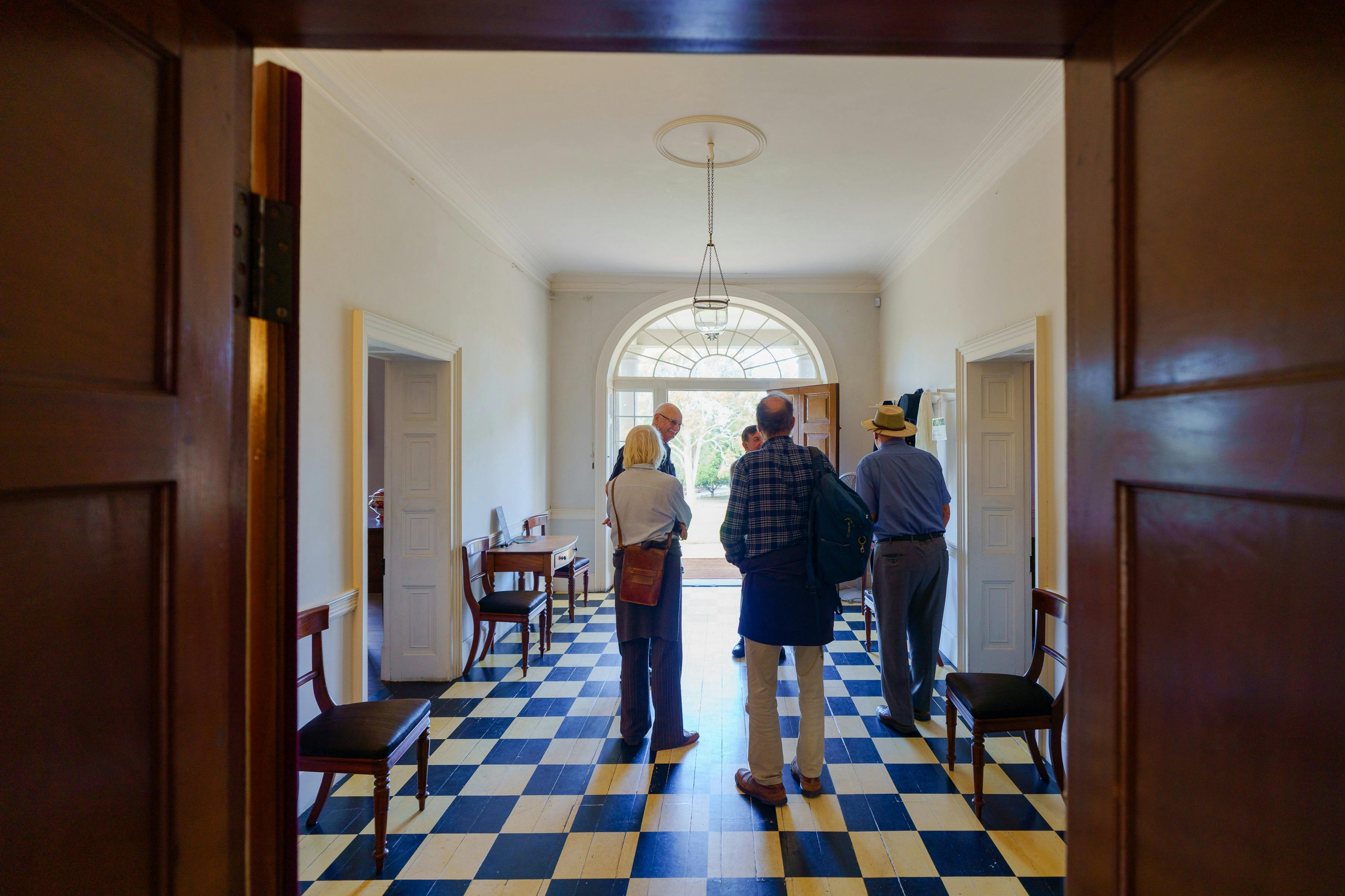 Group of people talking to guide in historic house foyer with checkered flooring