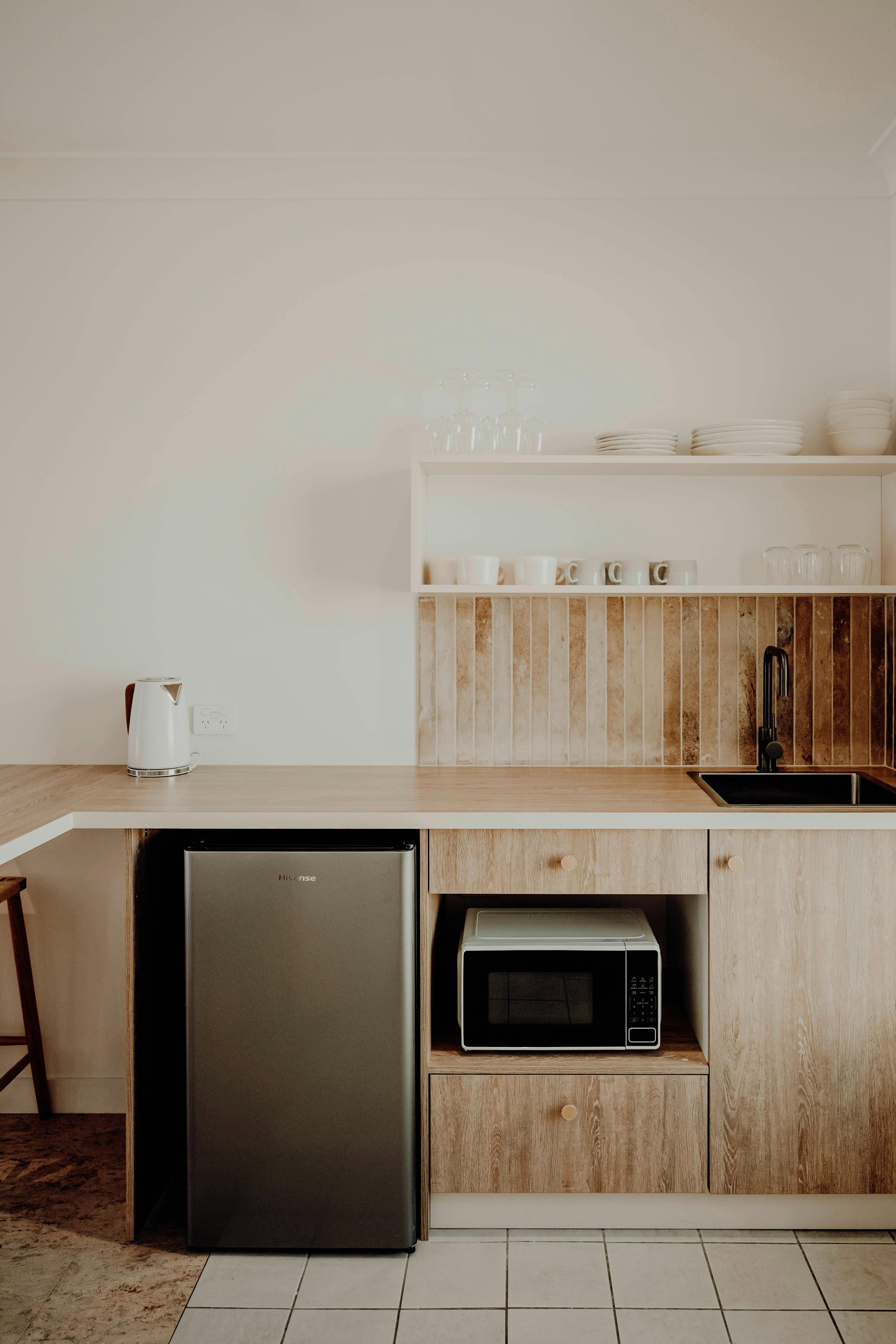 Kitchenette with smart shelves and tiling. Fridge, microwave and sink. Kettle and crockery.