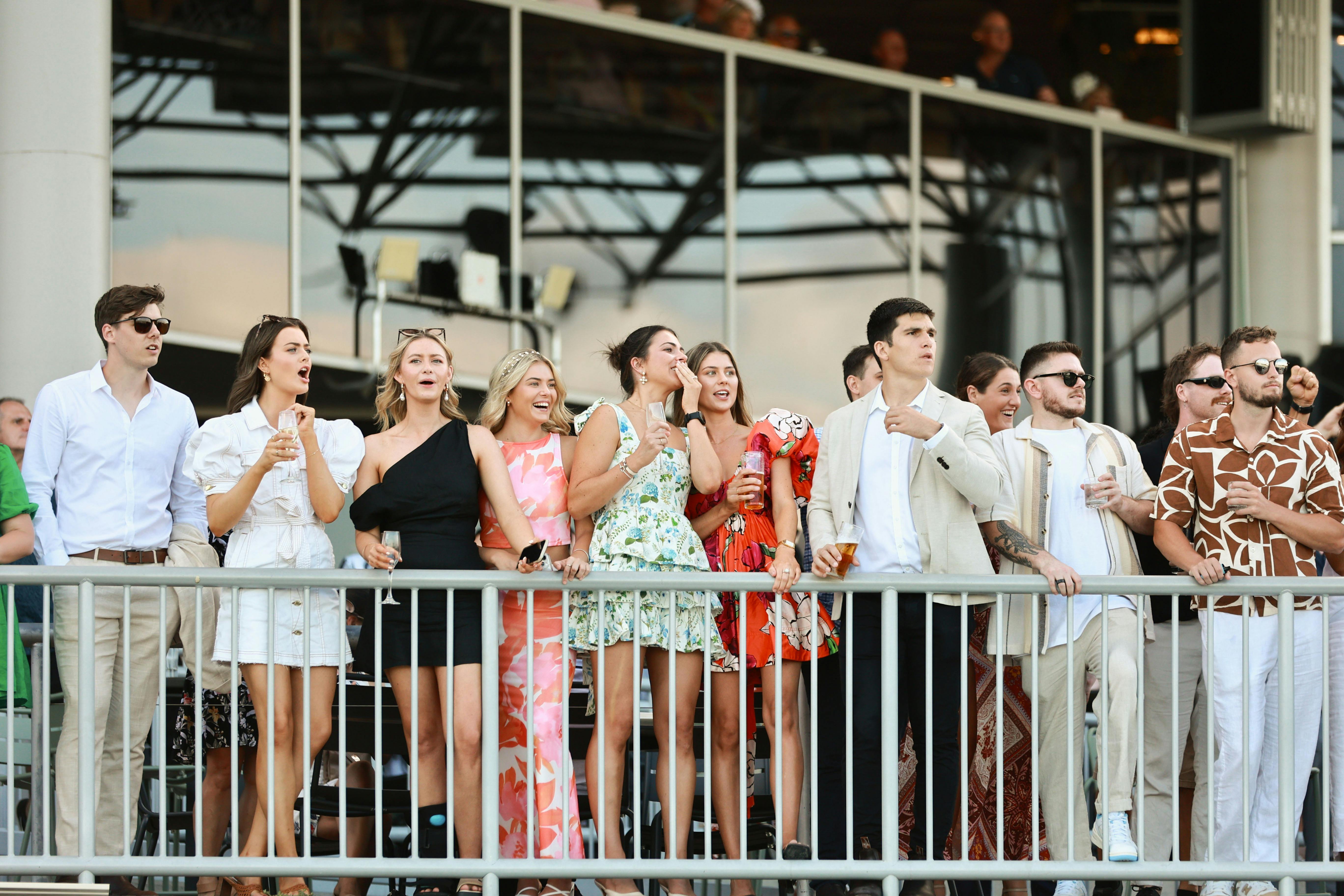 Group of friends lined up on a terrace fence cheering on the horses