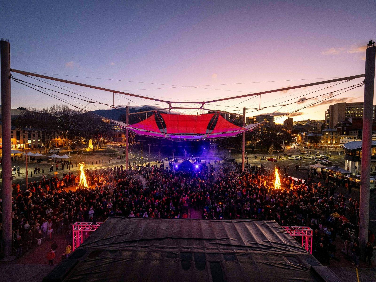 A colour phot showing the sun setting over the Big Sing event with live music and a big crowd