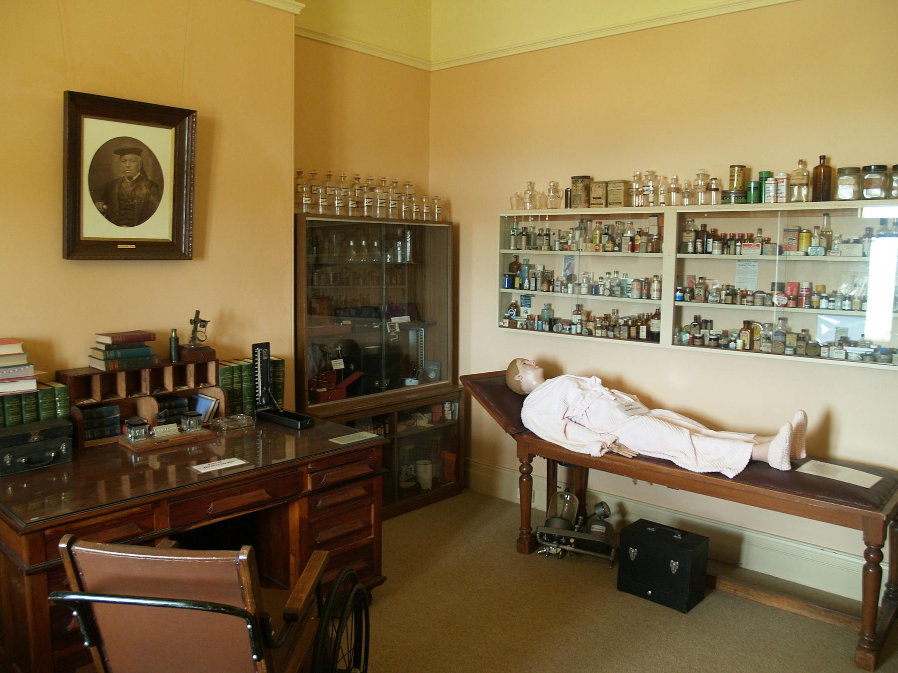 Medical room display of old bottles from a local chemist and a medical dummy on a patients couch