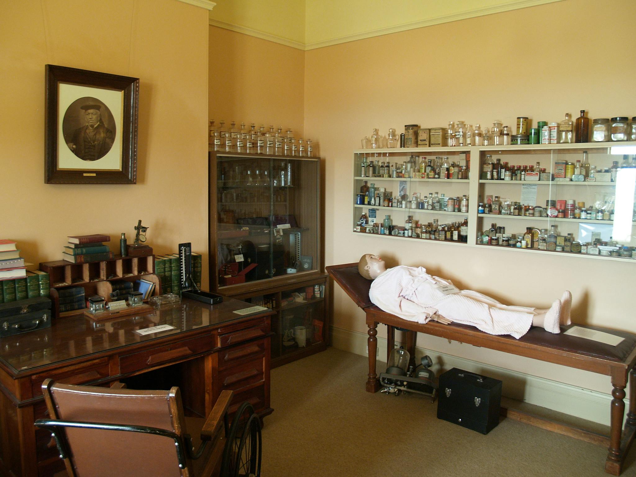 Medical room display of old bottles from a local chemist and a medical dummy on a patients couch