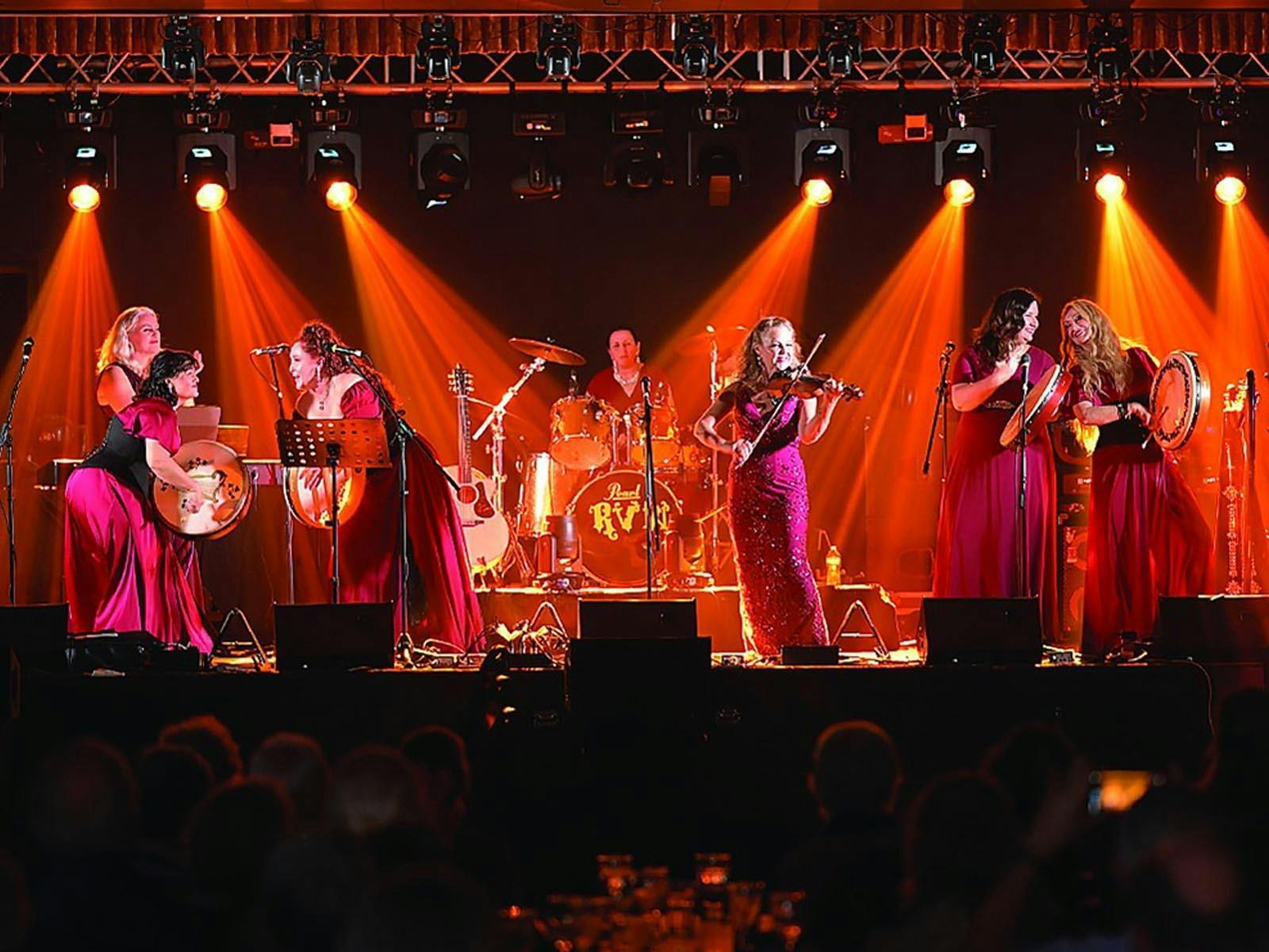 Women on a stage in red dresses playing traditional Irish instruments and singing