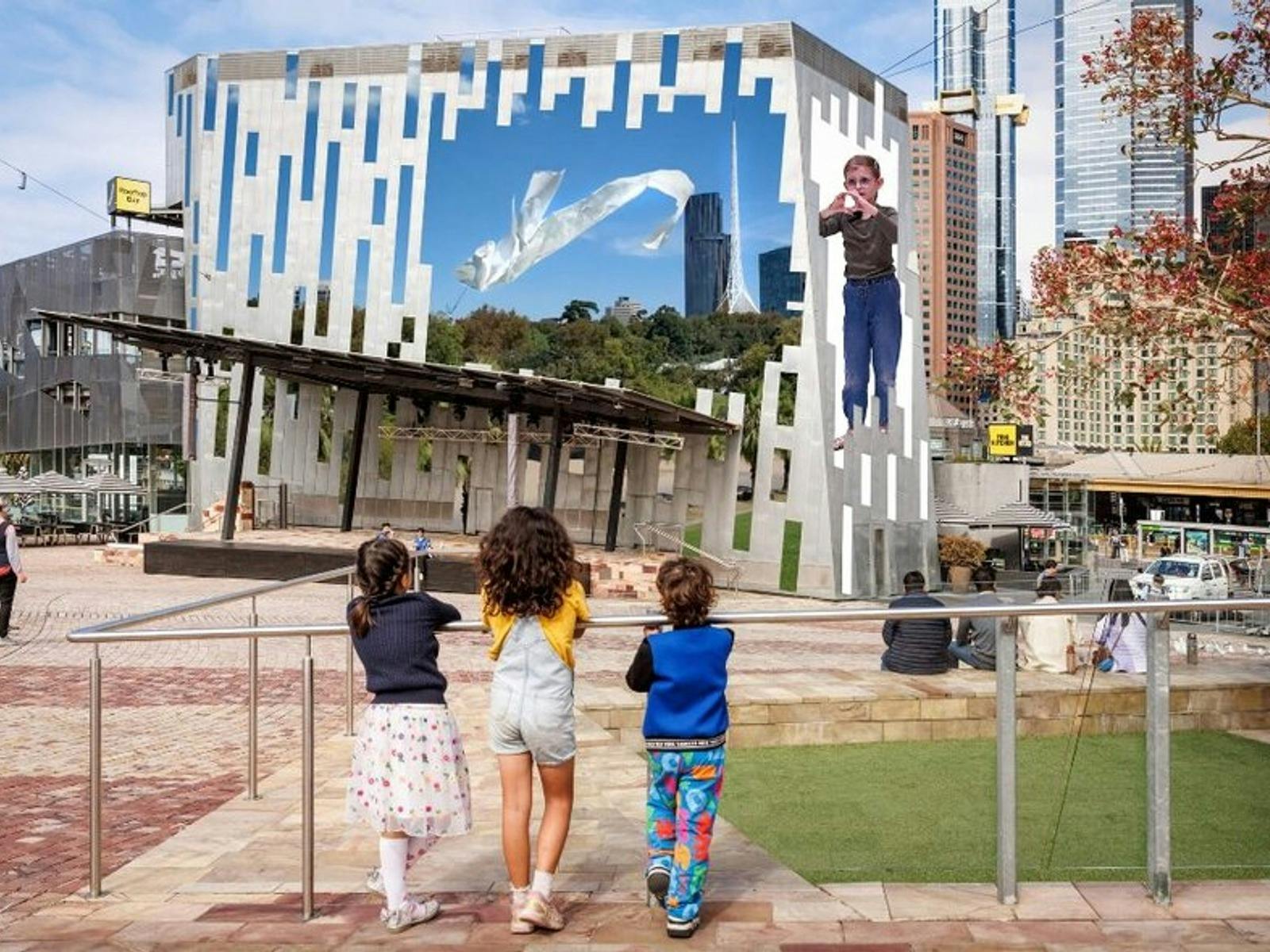 Three children face the main screen of Fed Square, with their backs to the camera