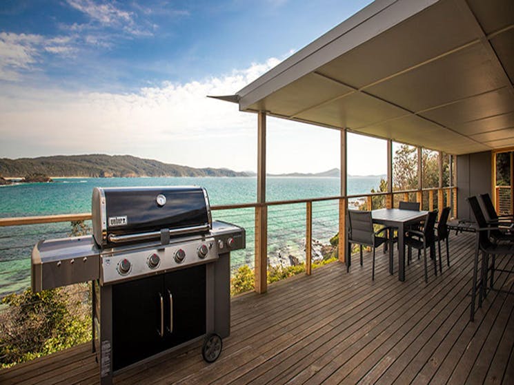 A gas barbecue and outdoor seating on the deck of Davies Cottage, with Sugarloaf Bay in the