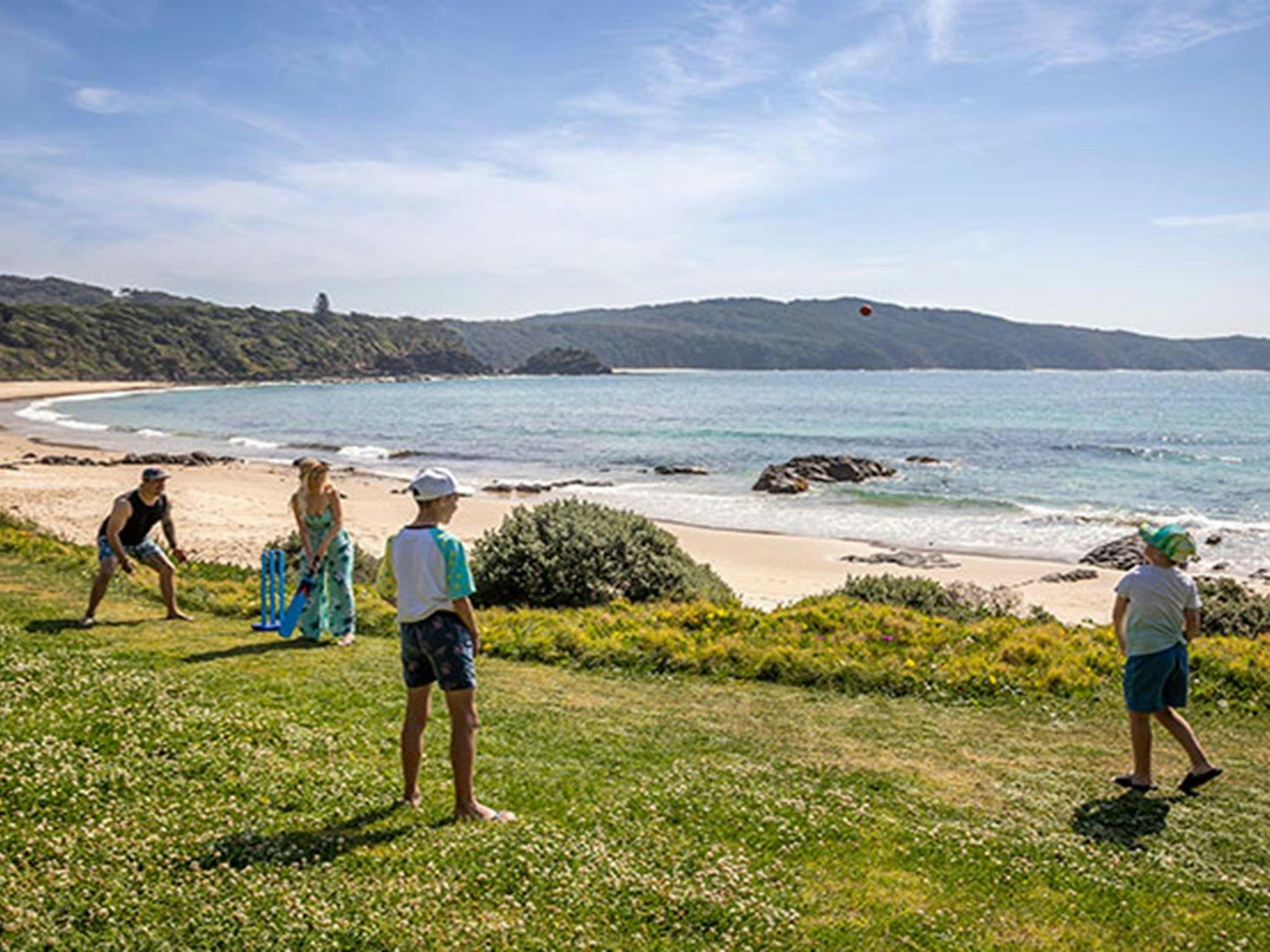 A family playing cricket on the grass below the cottage with Boat Beach in the background. Photo: